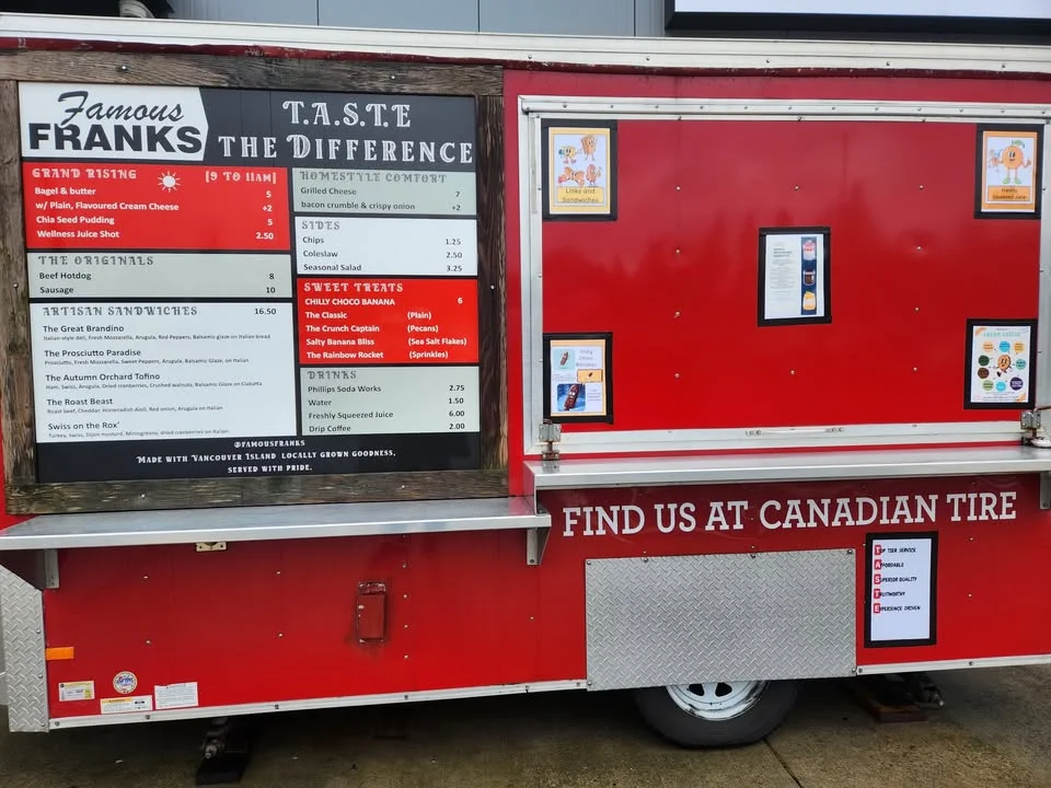 A red food truck featuring a menu board with various sandwiches, sides, and sweet treats. The truck is parked at a location, inviting customers.