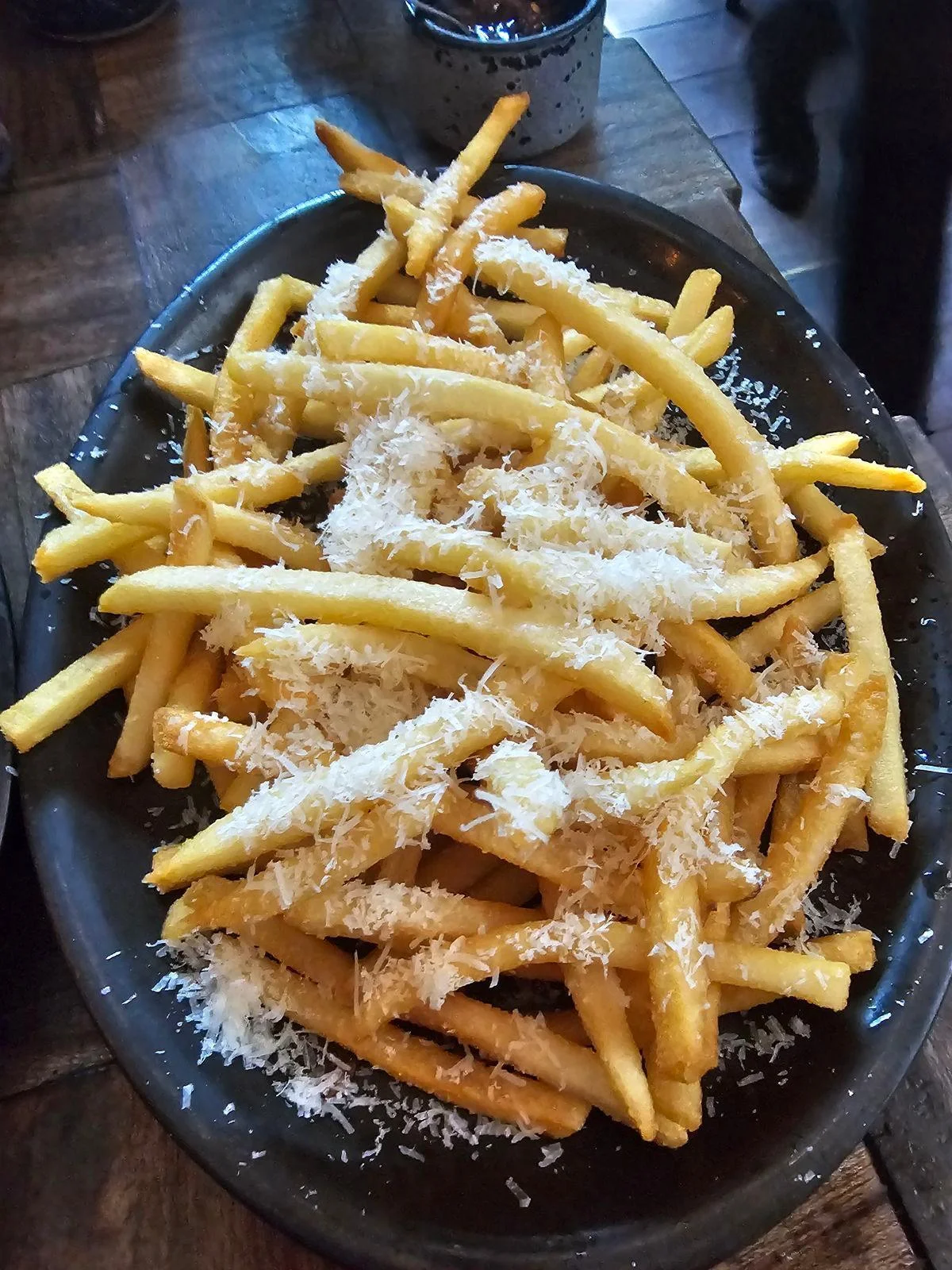 A generous serving of golden French fries topped with grated cheese, served on a black platter.
