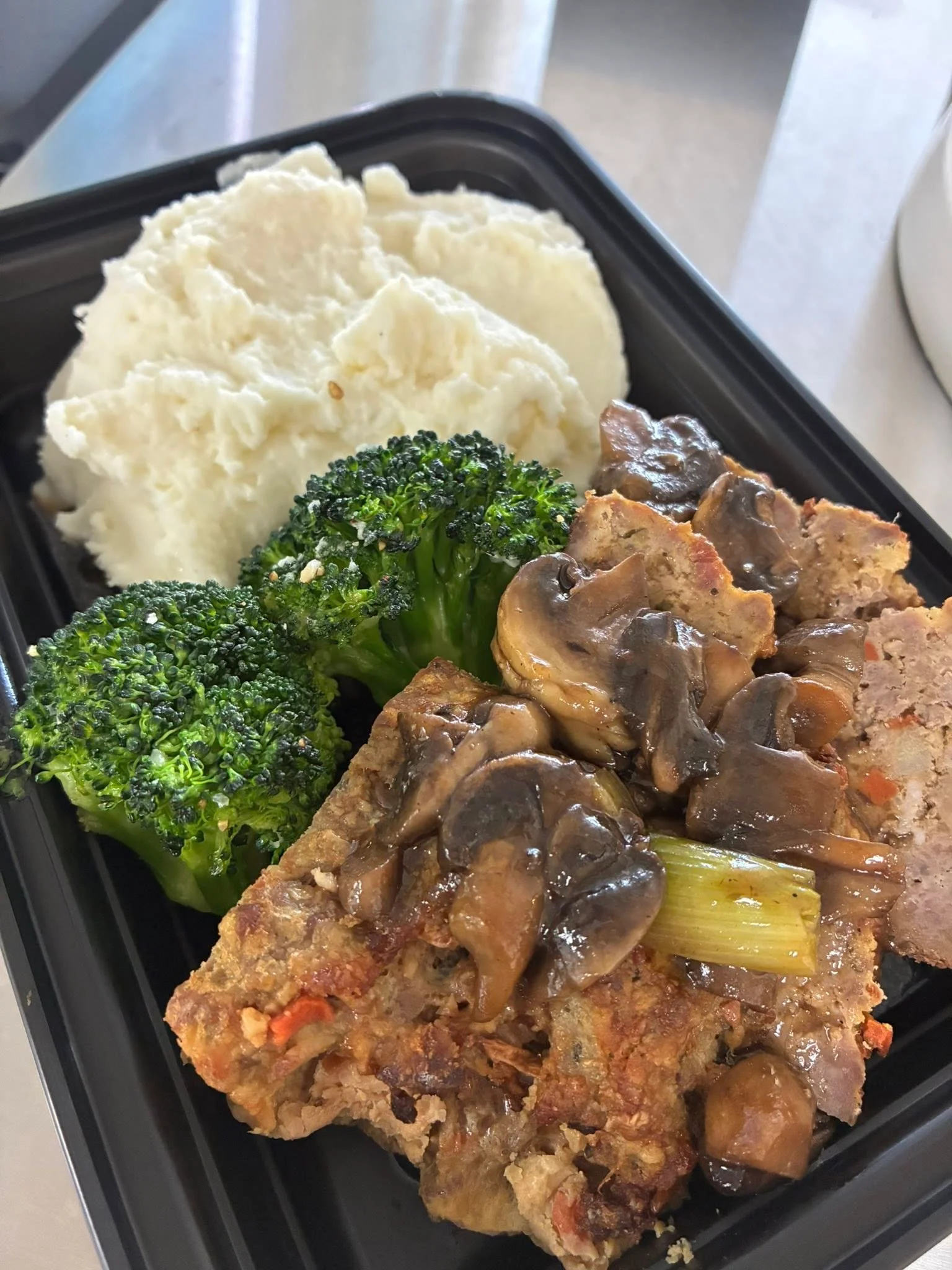 A meal featuring meatloaf, mashed potatoes, broccoli, and mushroom gravy.