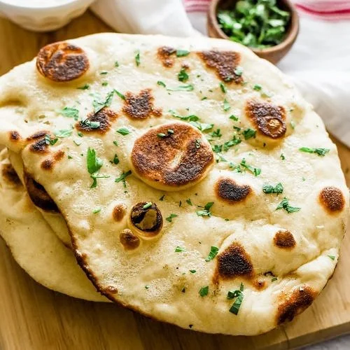 Delicious naan garlic bread with fresh herb toppings on a wooden table.