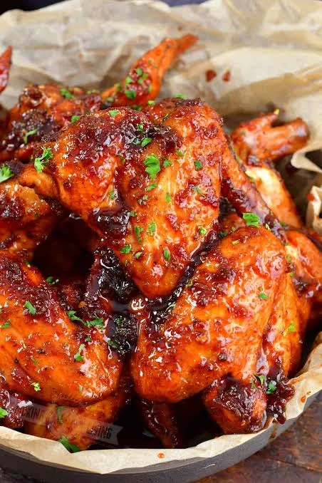 A platter of glazed chicken wings coated in a rich, sticky sauce, garnished with herbs.