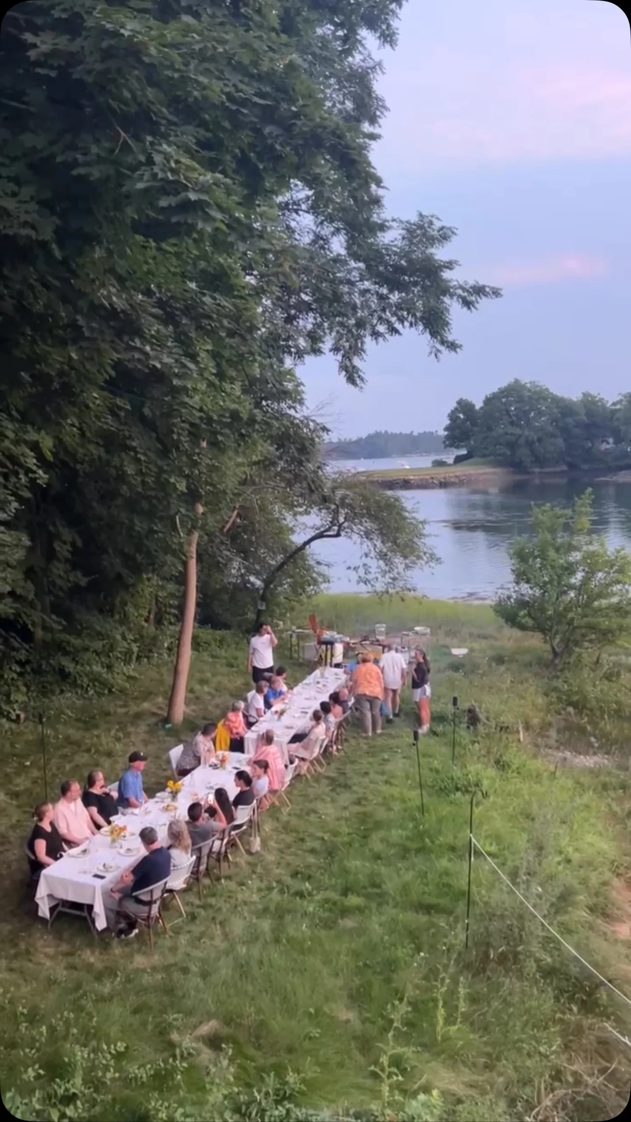 Outdoor dining event by the river with guests at a long table