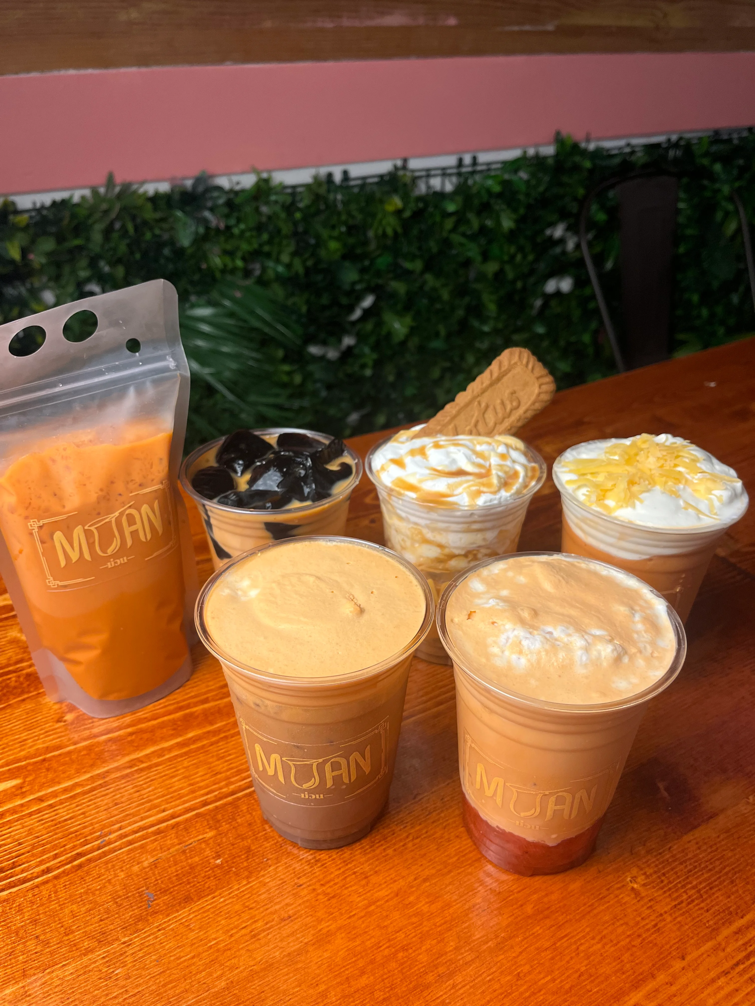 A variety of colorful drinks including iced beverages topped with whipped cream and syrup, along with a cup of jelly on a wooden table.