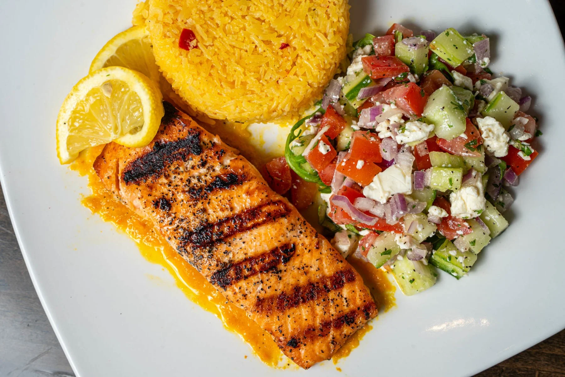 Grilled salmon with saffron rice and Mediterranean salad on a white plate