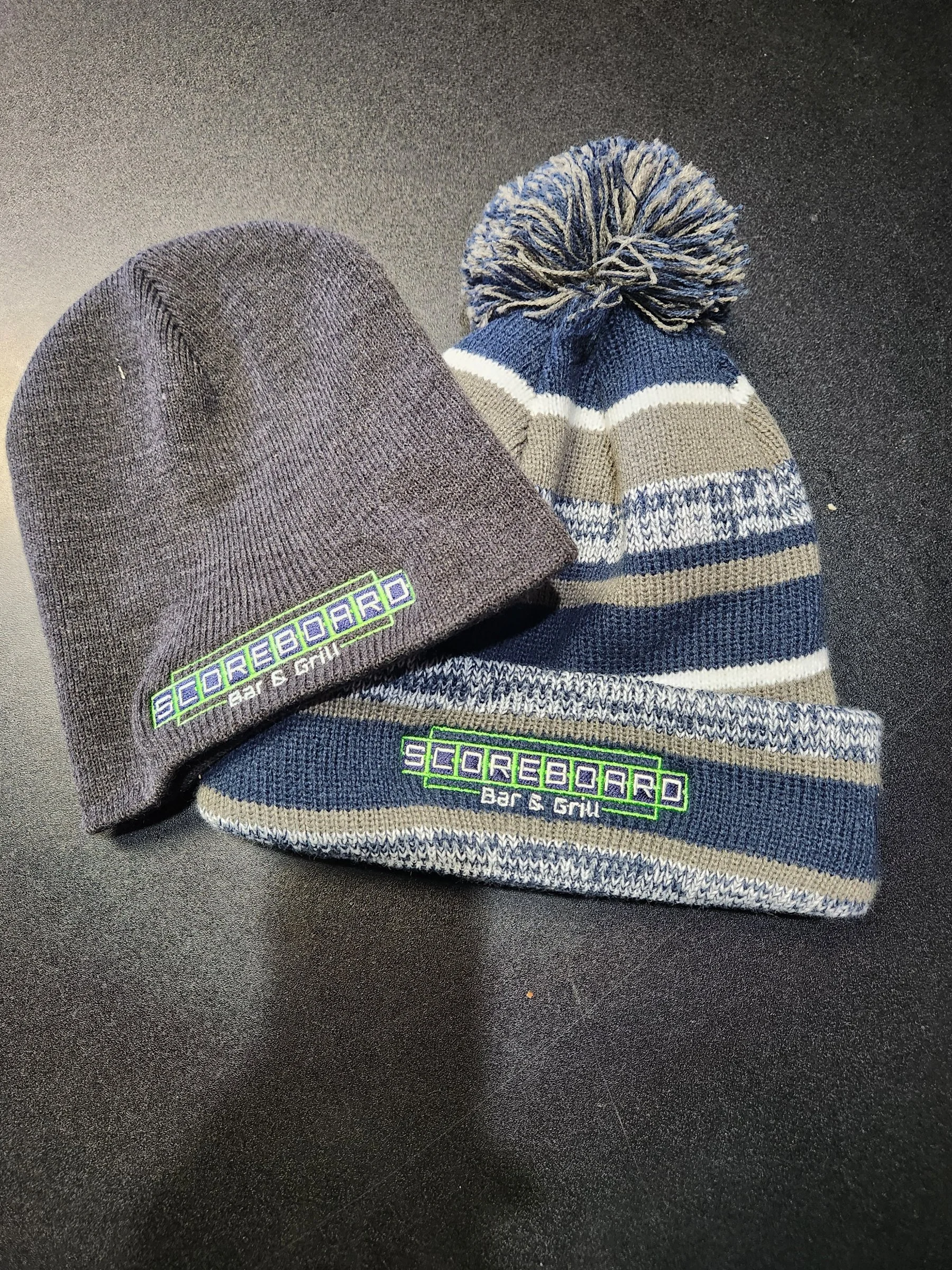 Two embroidered restaurant beanies displayed on a dark surface