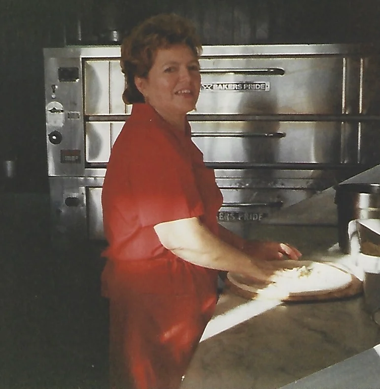 A person tossing pizza dough in a restaurant kitchen.