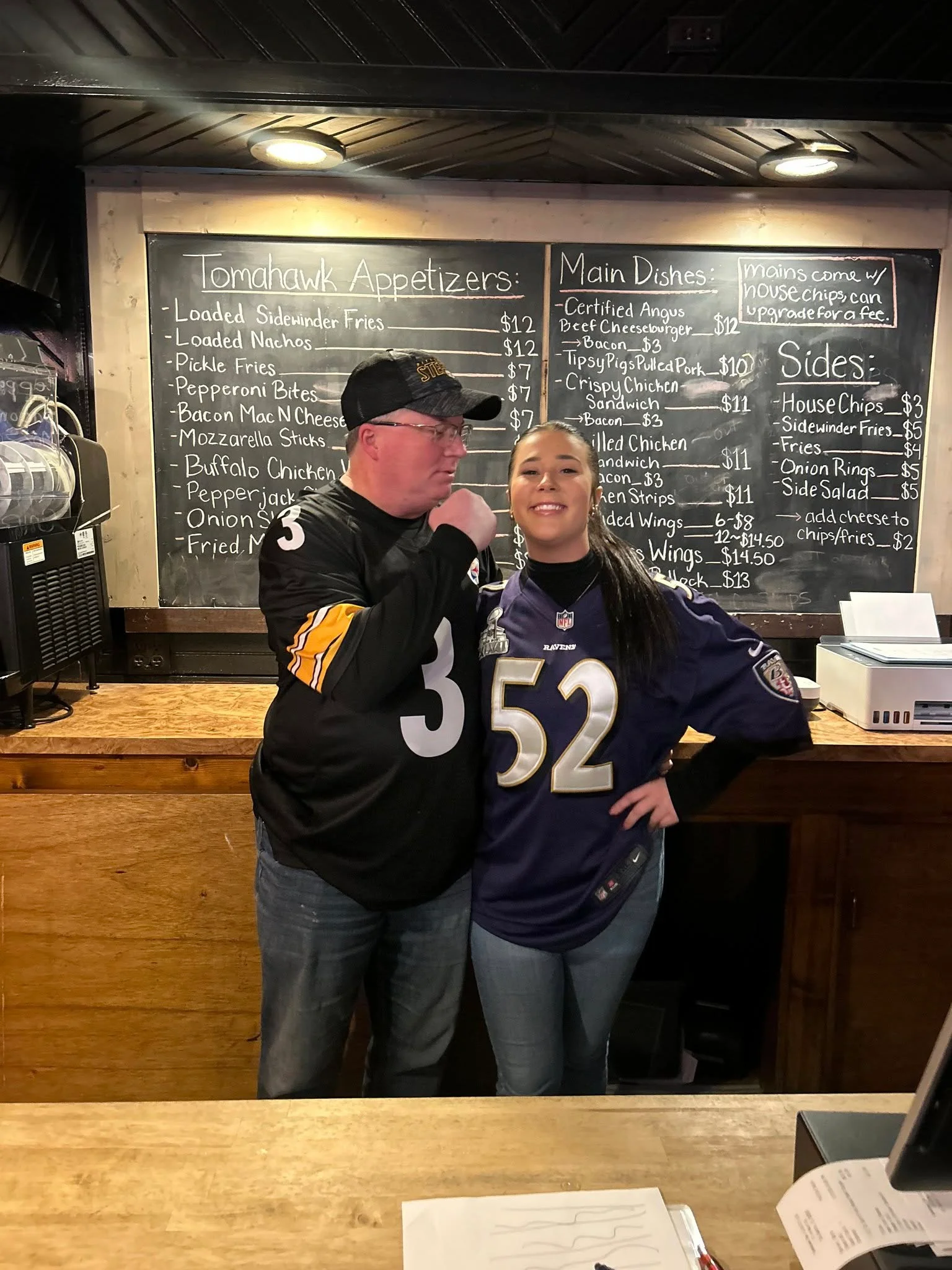 Friendly staff at a sports bar with a menu board in the background