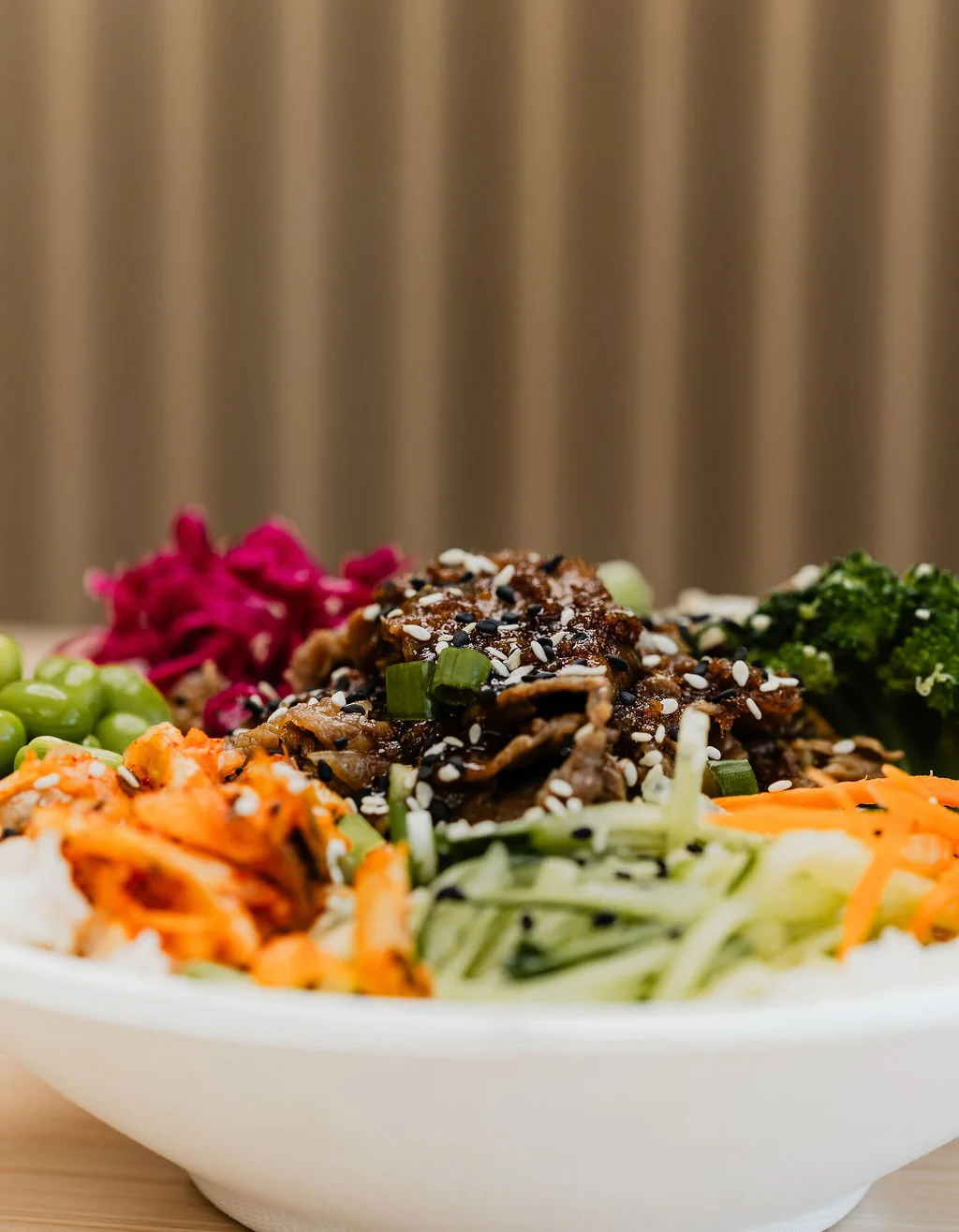 Bowl of rice topped with shaved ribeye, vegetables, and sauce