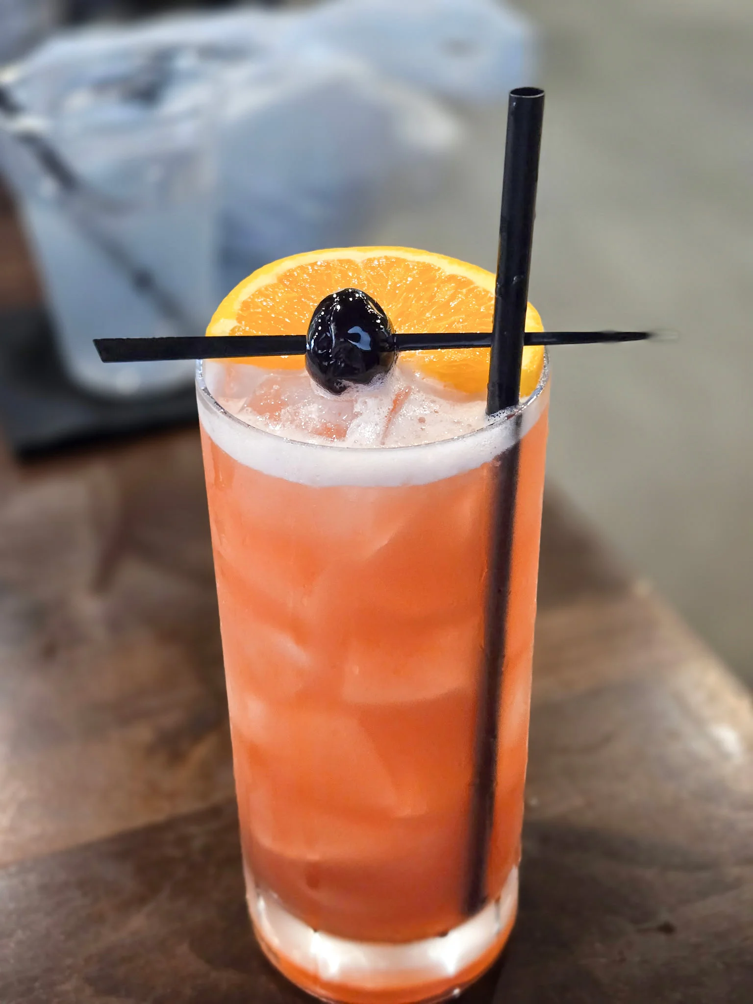 A vibrant cocktail garnished with an orange slice and a cherry, served in a tall glass.