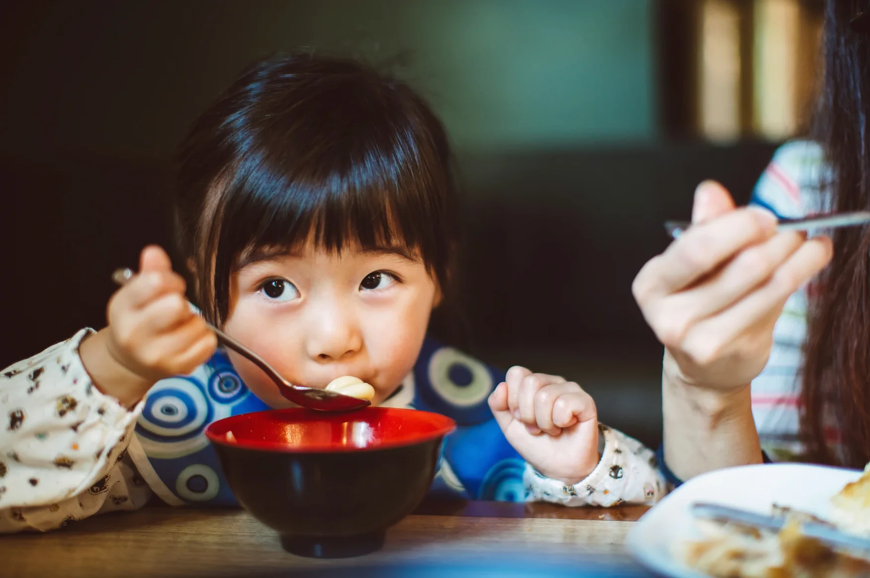 Child enjoying a bowl of Japanese ramen at a cozy dining table