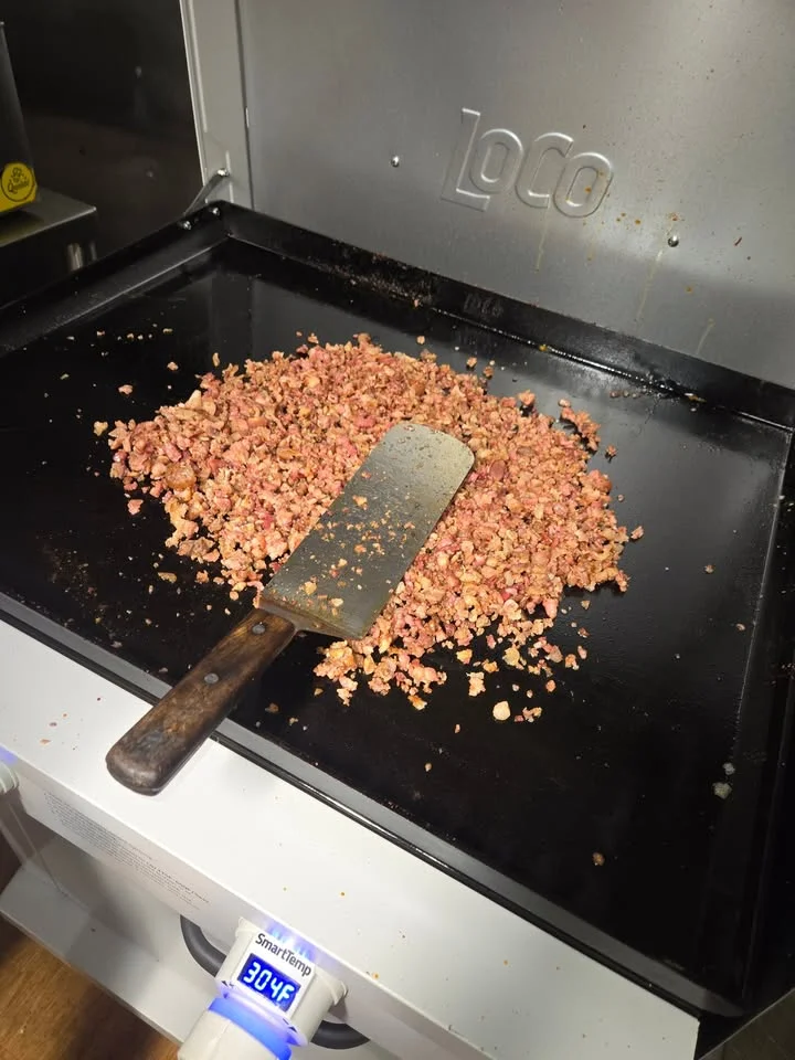 Sautéed ground meat on a griddle, with a spatula resting on top, showcasing a flavorful cooking process.