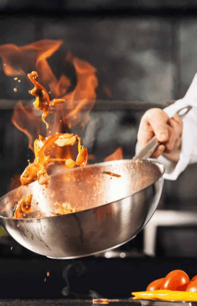 A chef skillfully tossing ingredients in a frying pan with flames erupting.