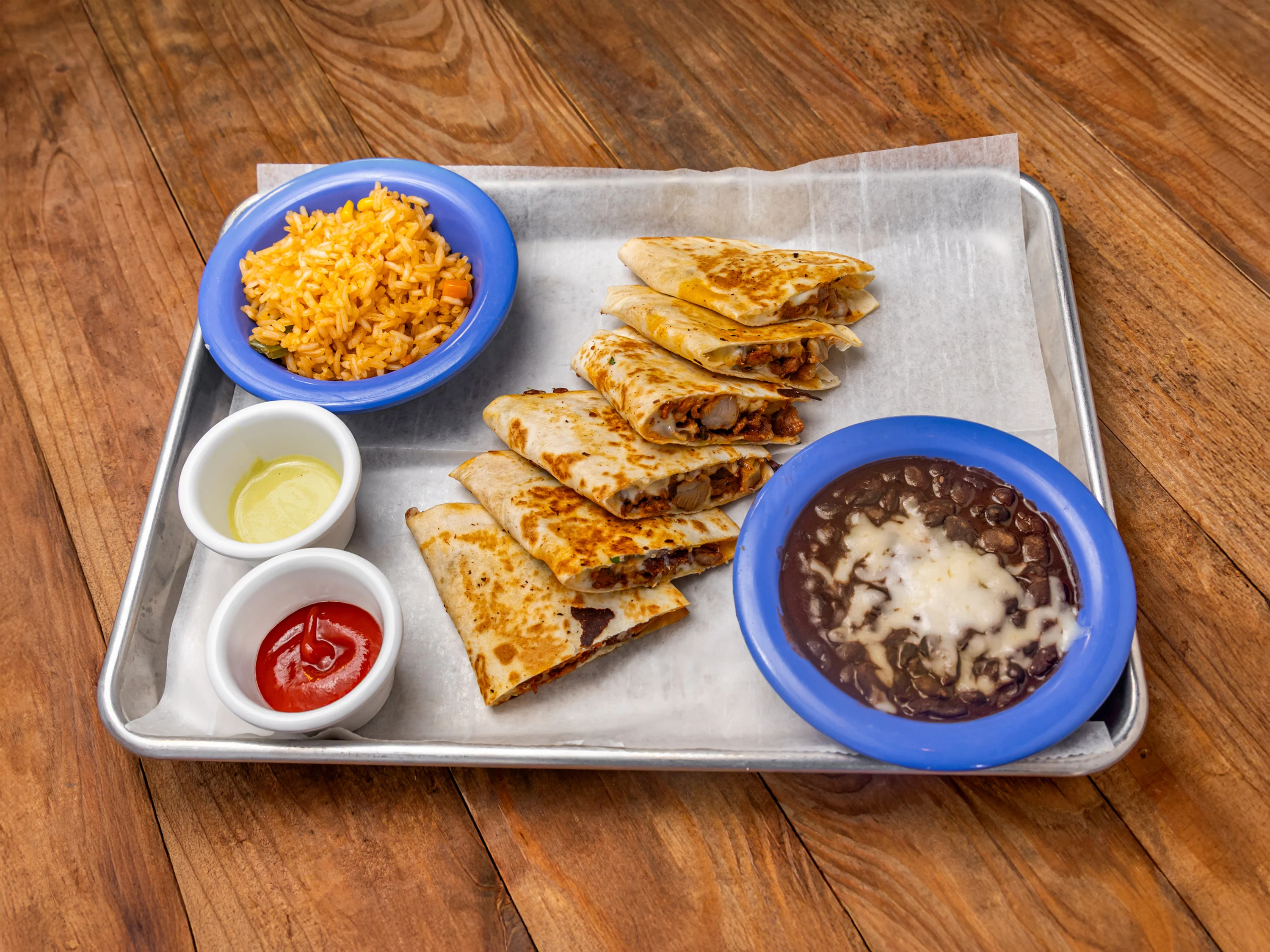 A plate featuring folded tortillas with fillings, accompanied by rice, black beans, and dipping sauces.