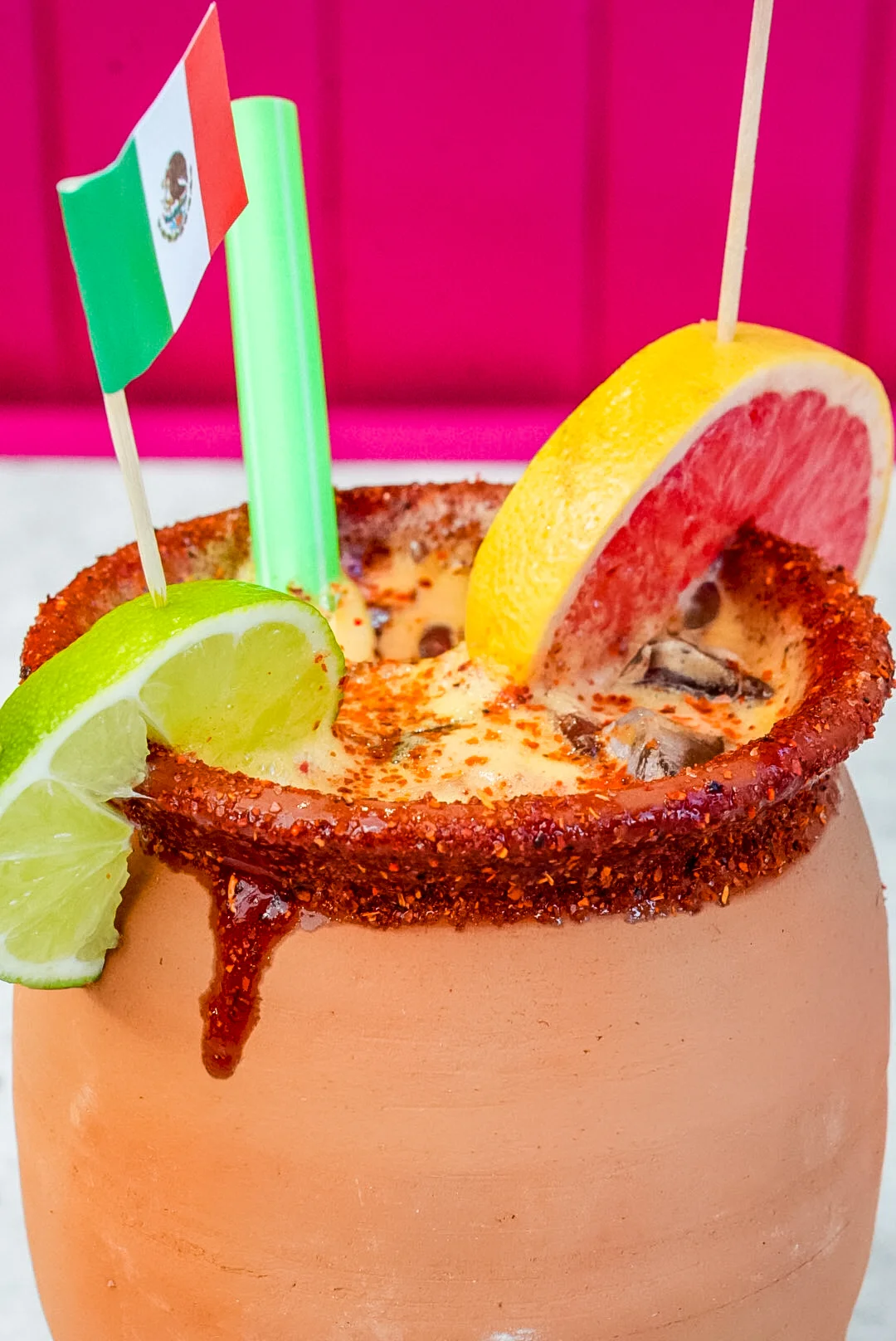 Colorful Mexican michelada in a clay mug with garnishes