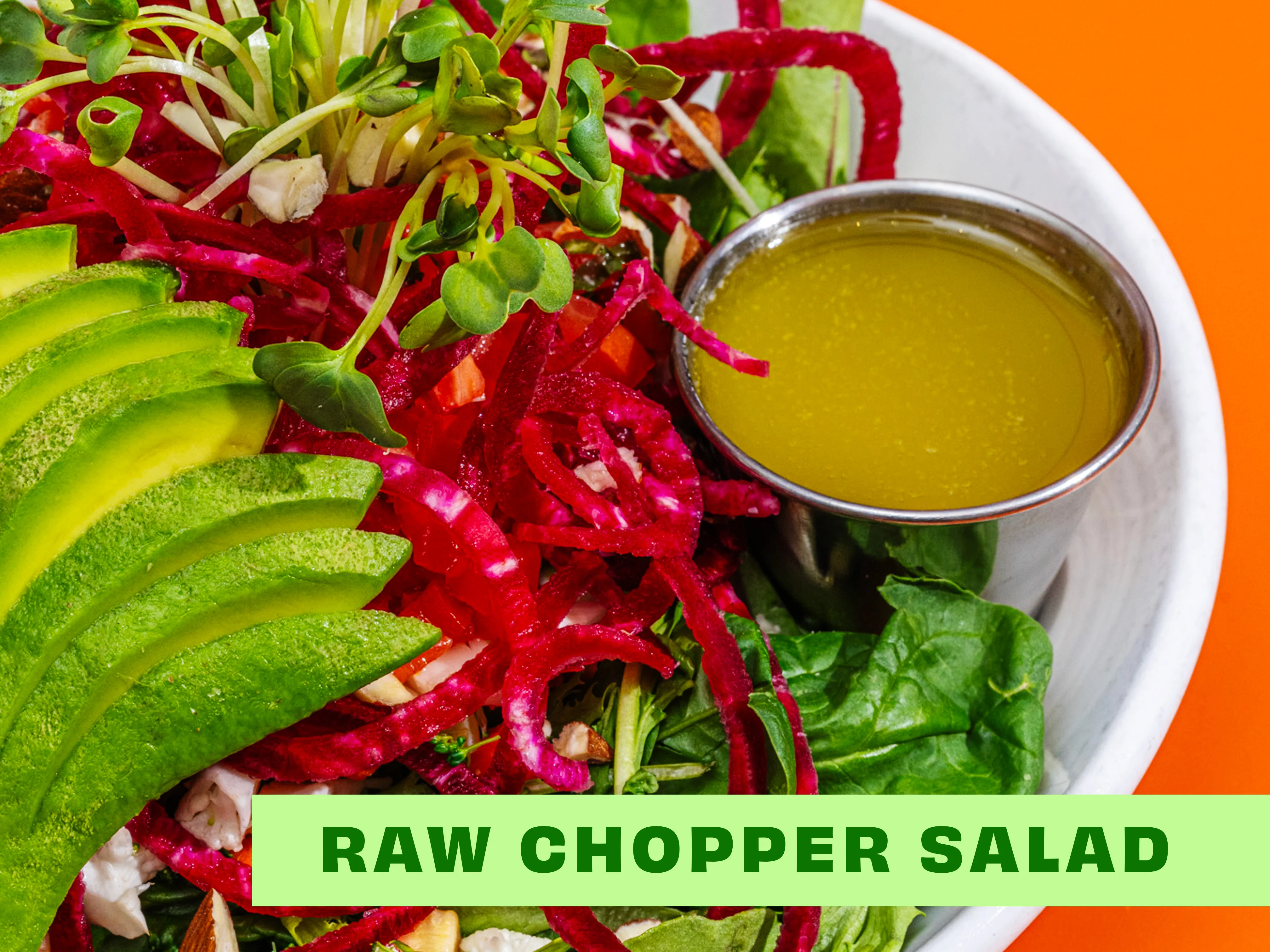 A colorful raw chopper salad adorned with fresh greens, sliced avocado, and a small serving of dressing on the side.