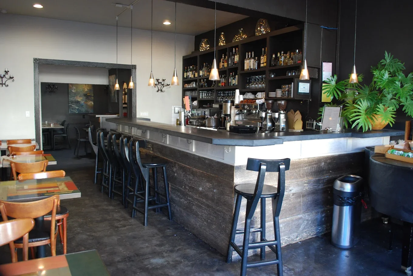 An interior view of a bar area with a dark wood counter, shelves of liquor, and hanging lights creating a cozy ambiance.