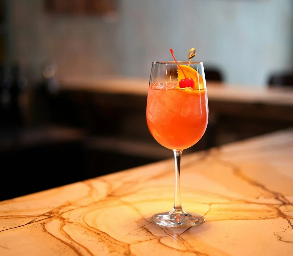A vibrant cocktail with ice and an orange twist on a marble table.