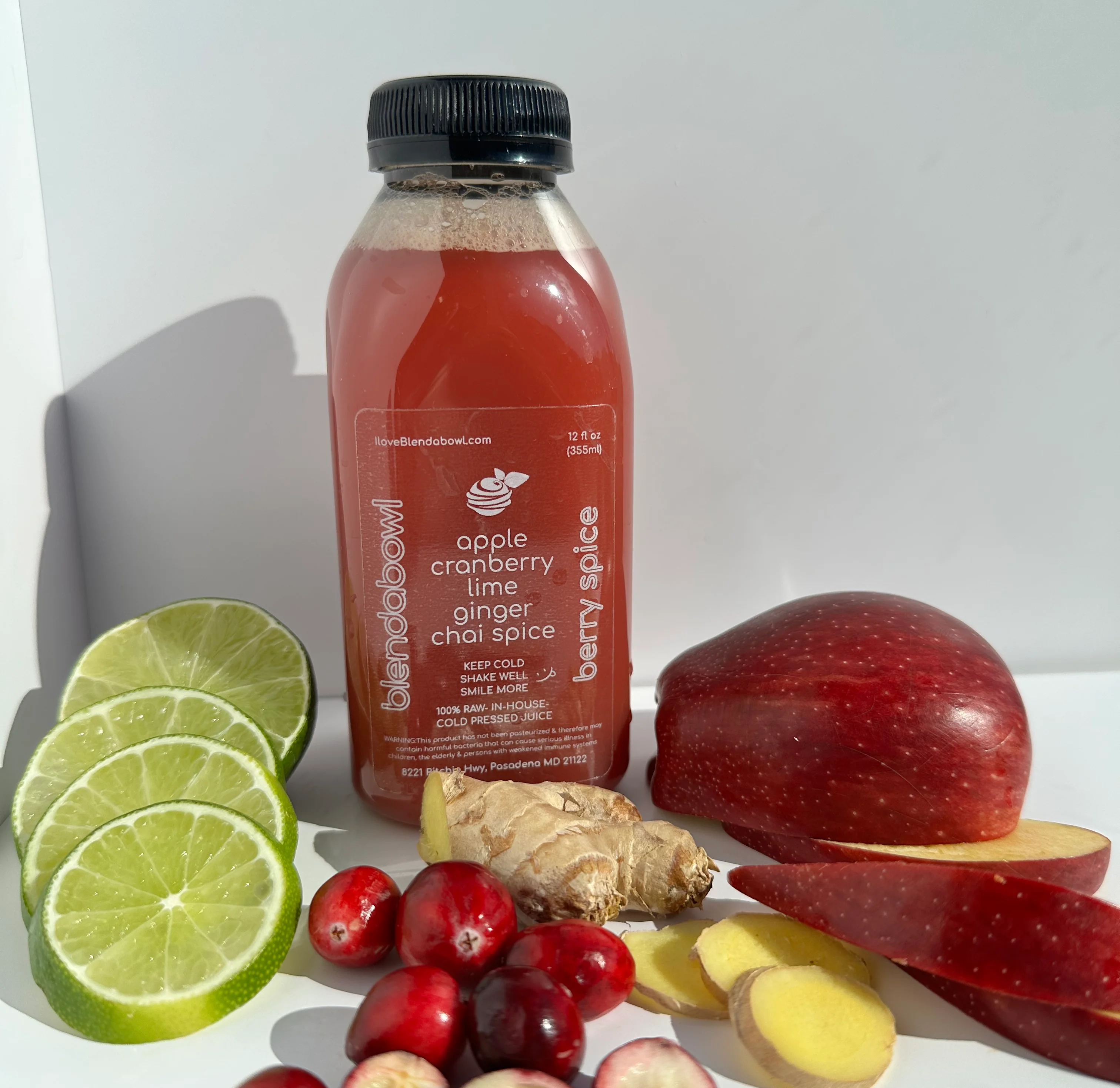 Juice bottle with lime, cranberry, ginger and apple surrounding it.