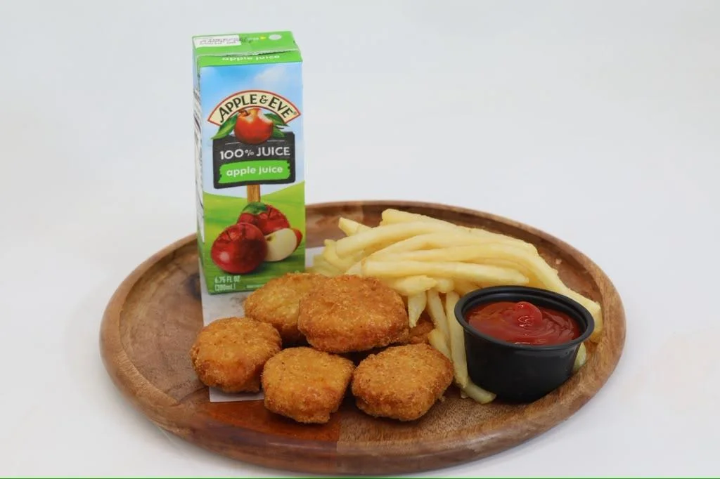 A wooden plate featuring chicken nuggets, French fries, and a small cup of ketchup, accompanied by a carton of apple juice.