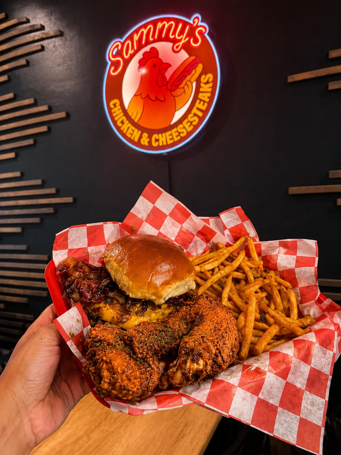 A basket filled with a sandwich, fried chicken, and fries, showcased on red and white checkered paper.