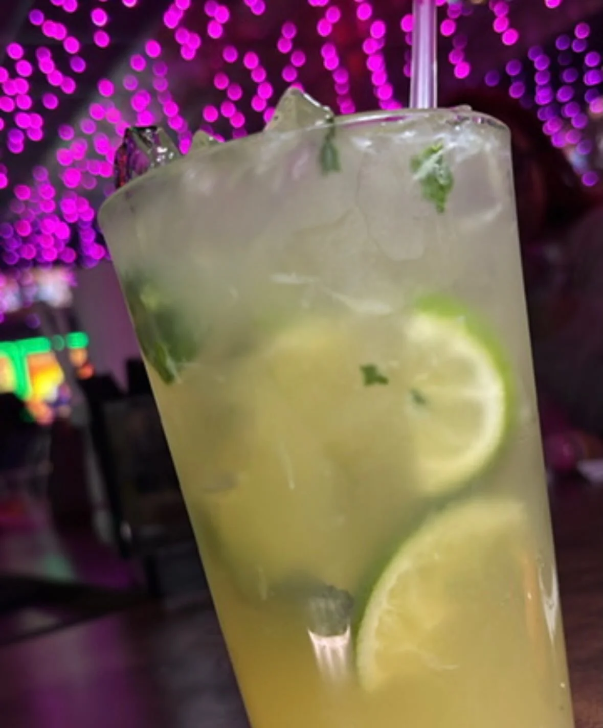 A refreshing drink with lime slices and mint leaves, served in a tall glass with ice, set against a backdrop of purple lights.