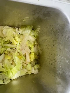A sink filled with discarded lettuce leaves, showing remnants of food preparation.
