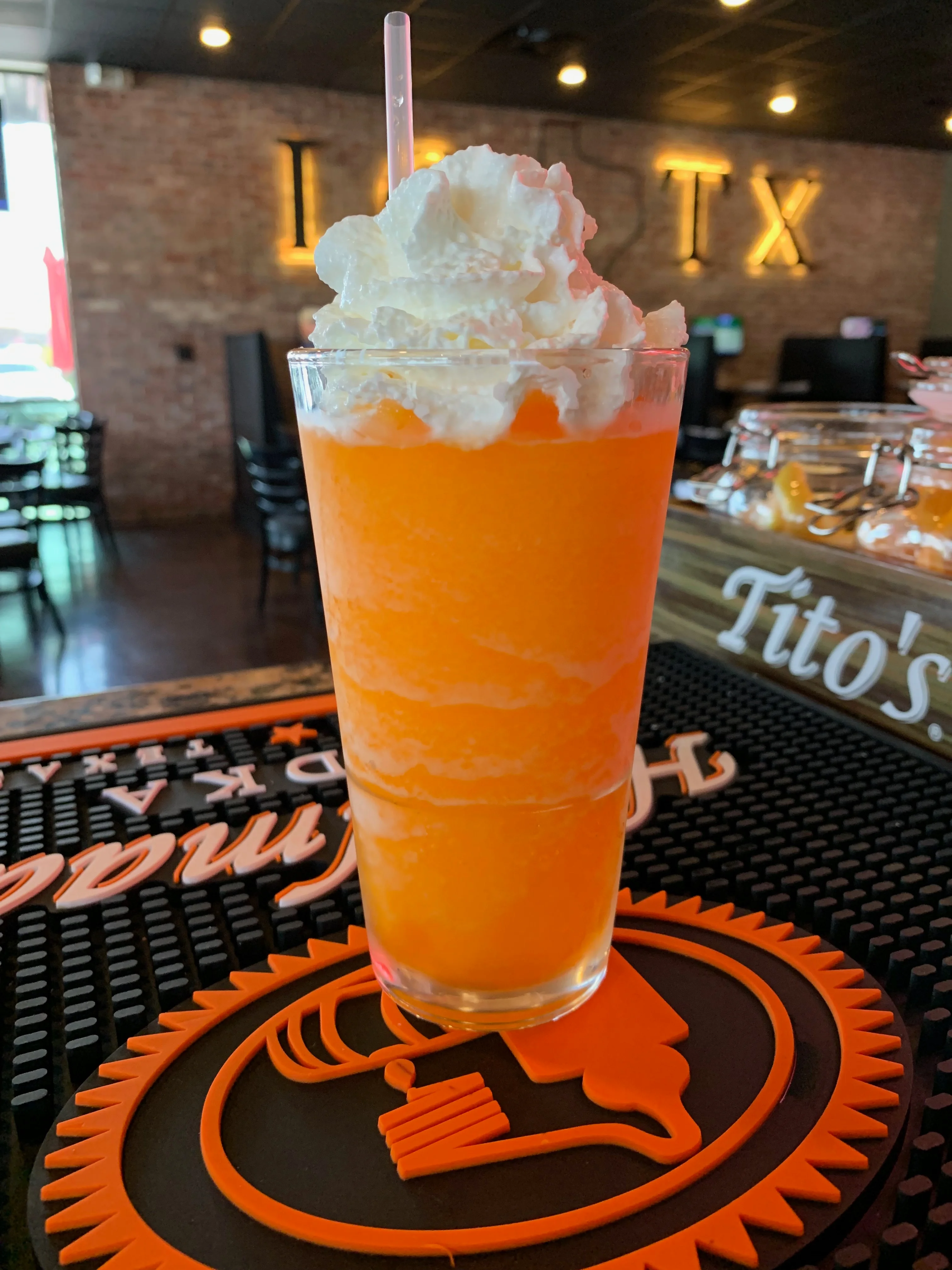 A refreshing orange slushy drink topped with whipped cream and served in a tall glass with a straw.