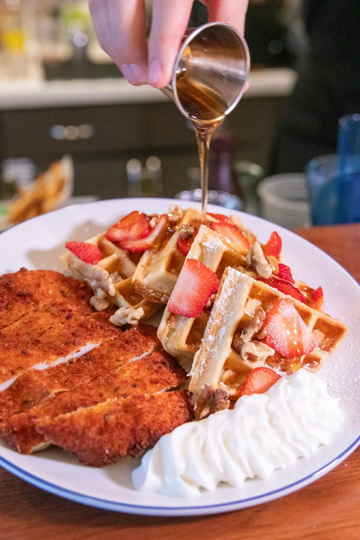Plate of chicken and waffles topped with strawberries and syrup.