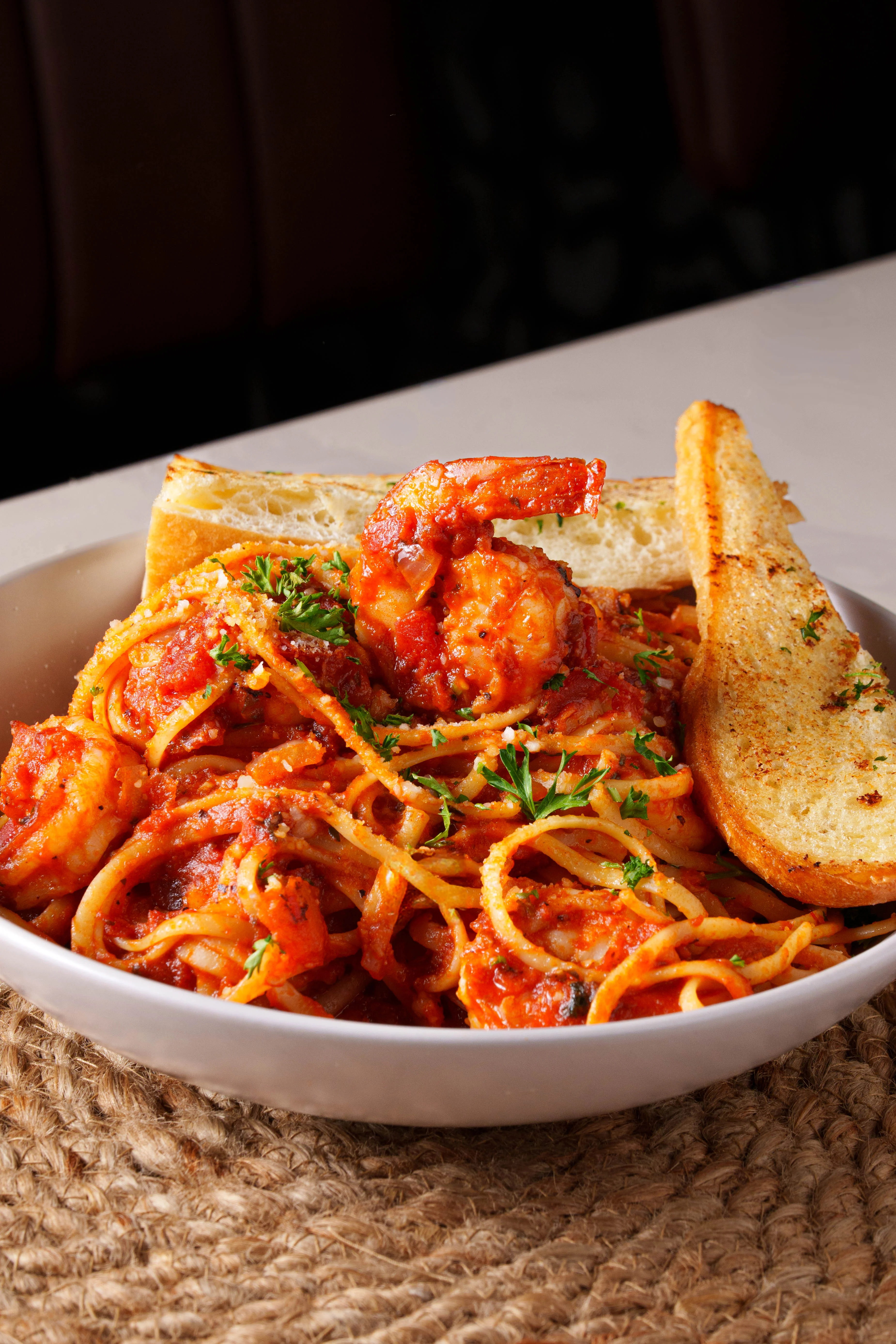 A bowl of penne pasta tossed in a vibrant red sauce, garnished with fresh herbs, served on a white plate against a wooden backdrop.