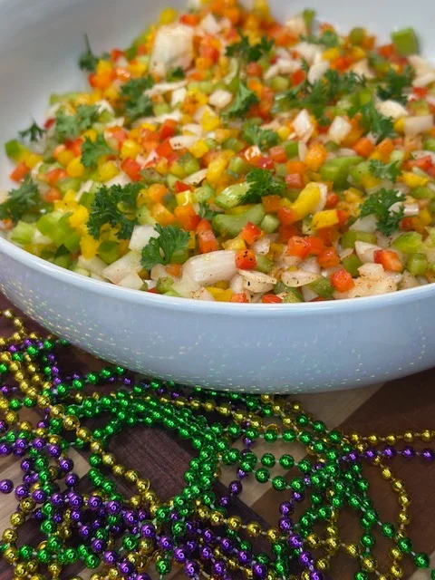 A colorful salad made of diced vegetables including peppers and onions, garnished with parsley, placed in a white bowl.