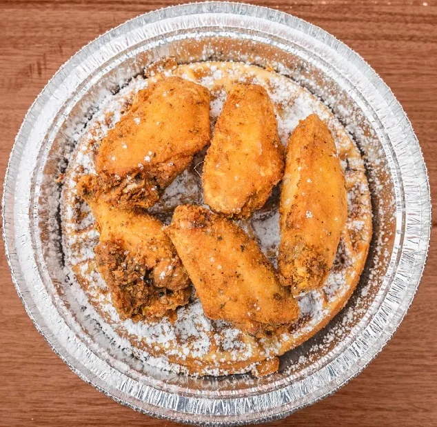 A dish containing fried chicken wings placed on top of a waffle and dusted with powdered sugar.