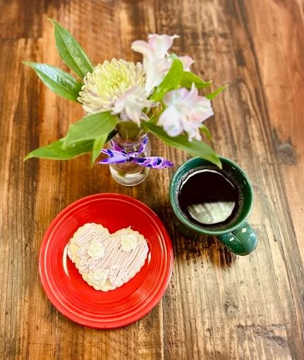 Heart-shaped cookie on a red plate with coffee and flowers