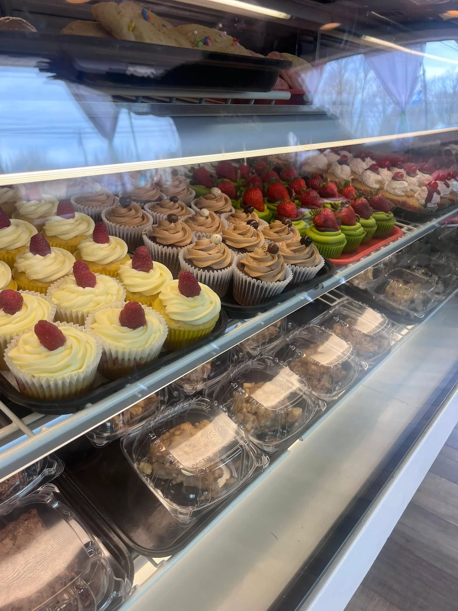 Display case with assorted cupcakes and desserts, including chocolate and fruit toppings.