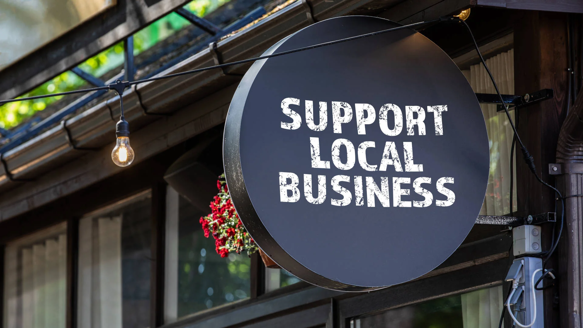 Sign promoting support for local businesses with vibrant greenery in the background