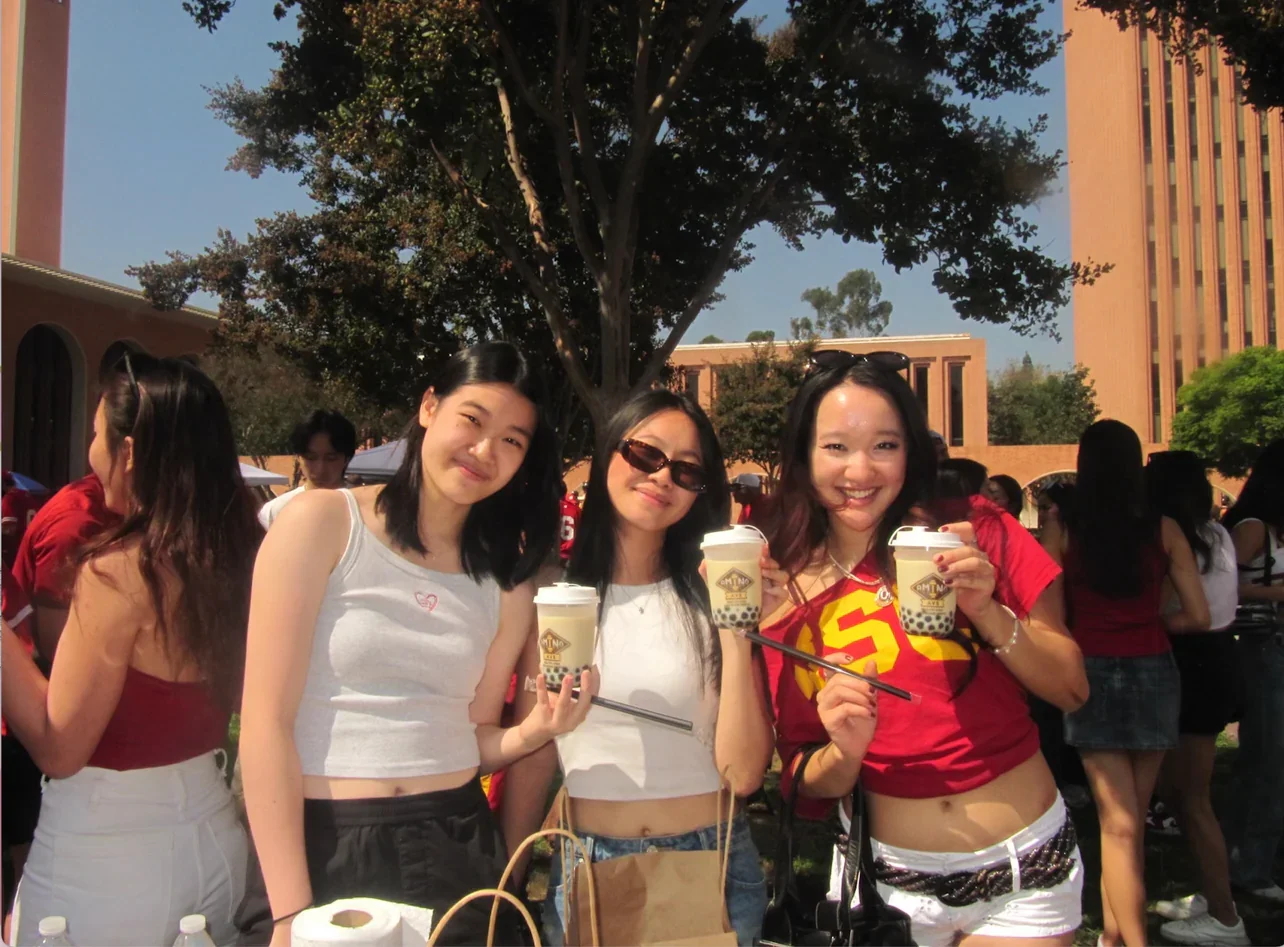 Three friends enjoying bubble tea at a lively outdoor event