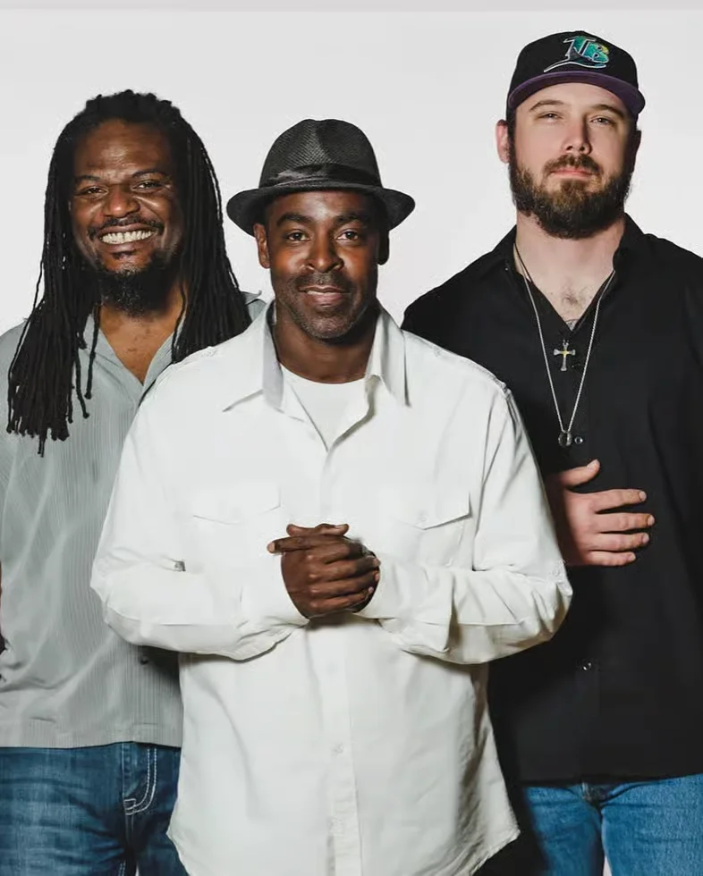 Three musicians posing together with smiles against a white background
