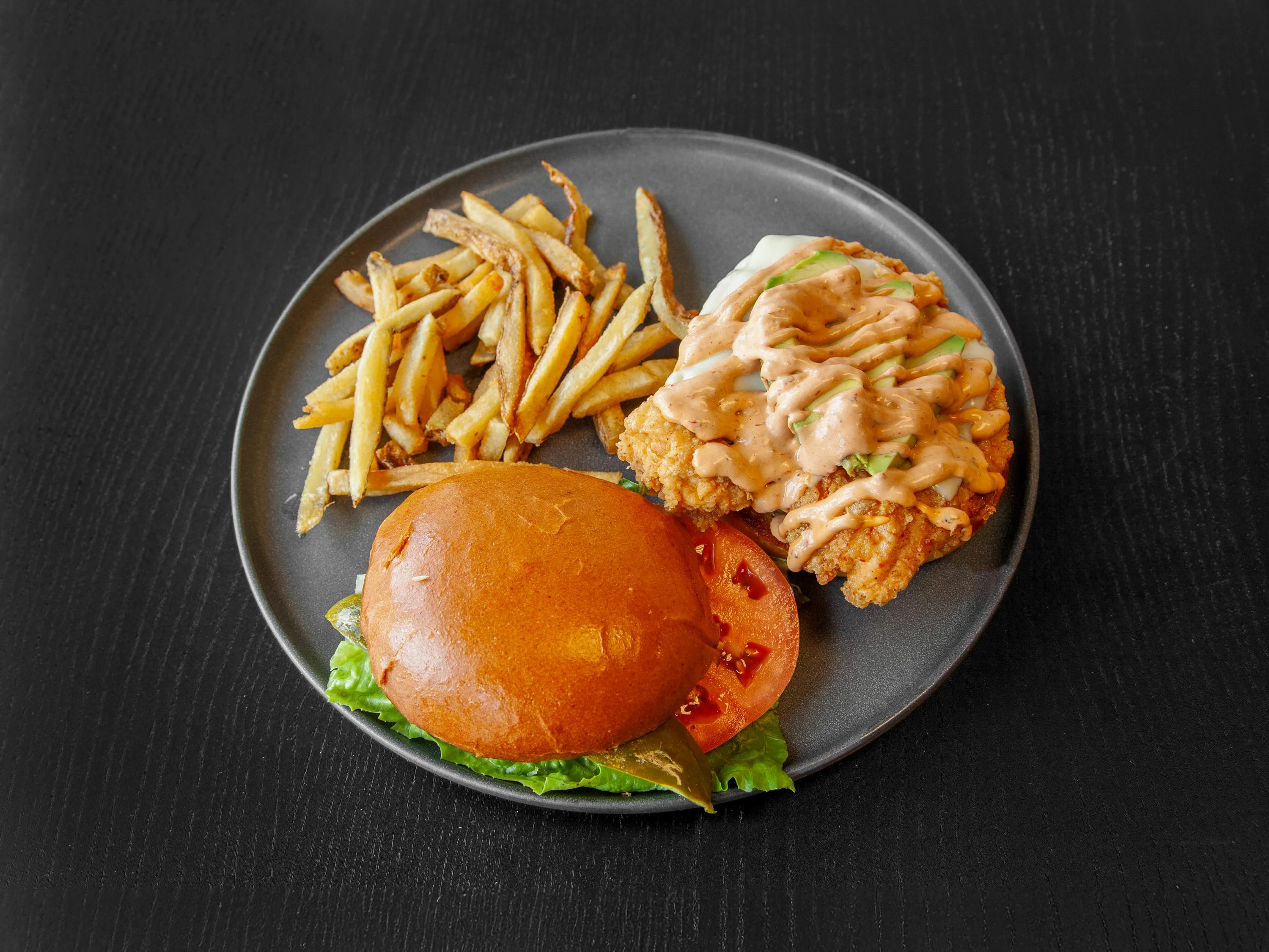 A plate featuring a crispy chicken sandwich with sauce, lettuce, and tomato, accompanied by a side of crispy fries.
