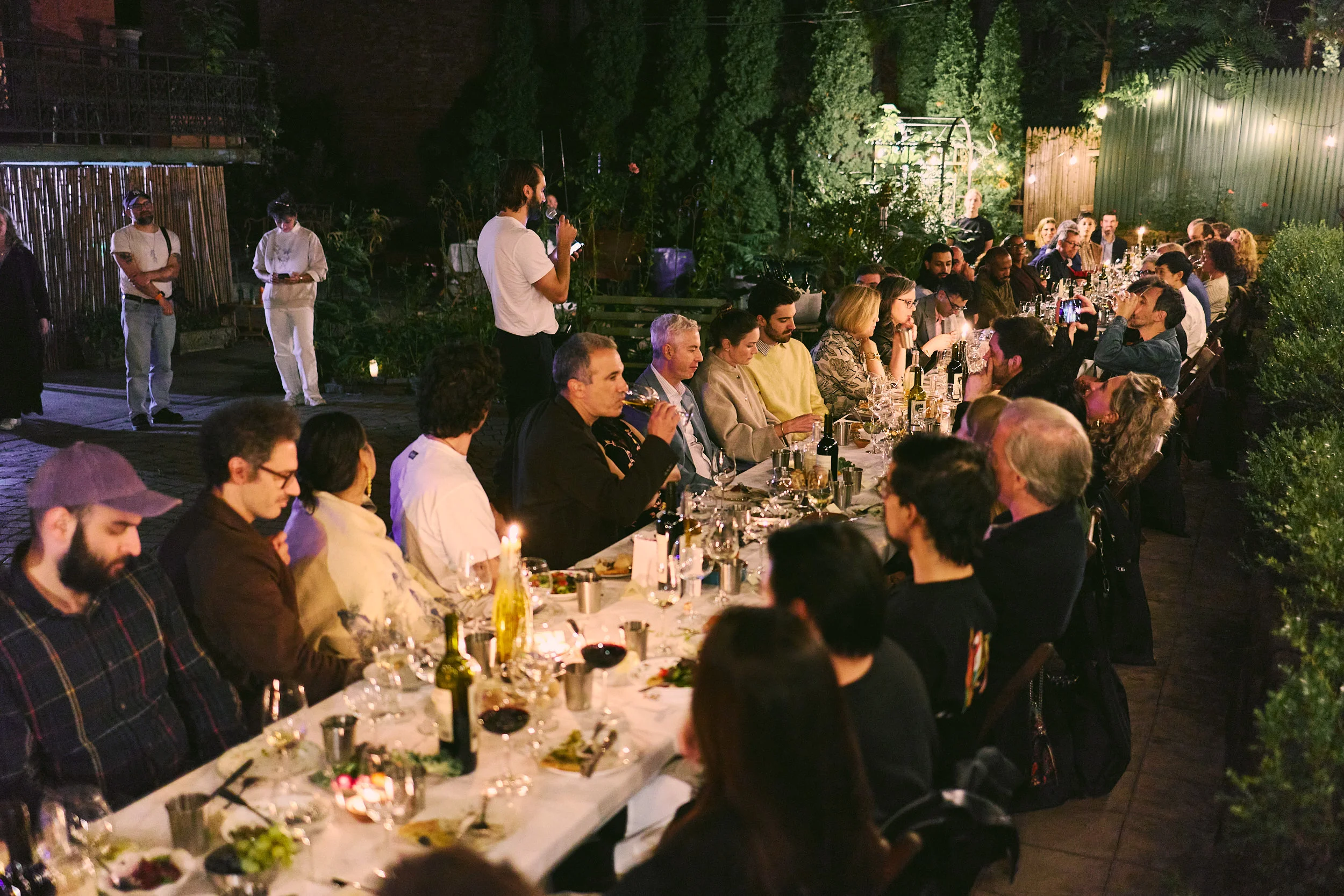 Elegant outdoor restaurant dinner with guests, wine, candles, and garden lighting