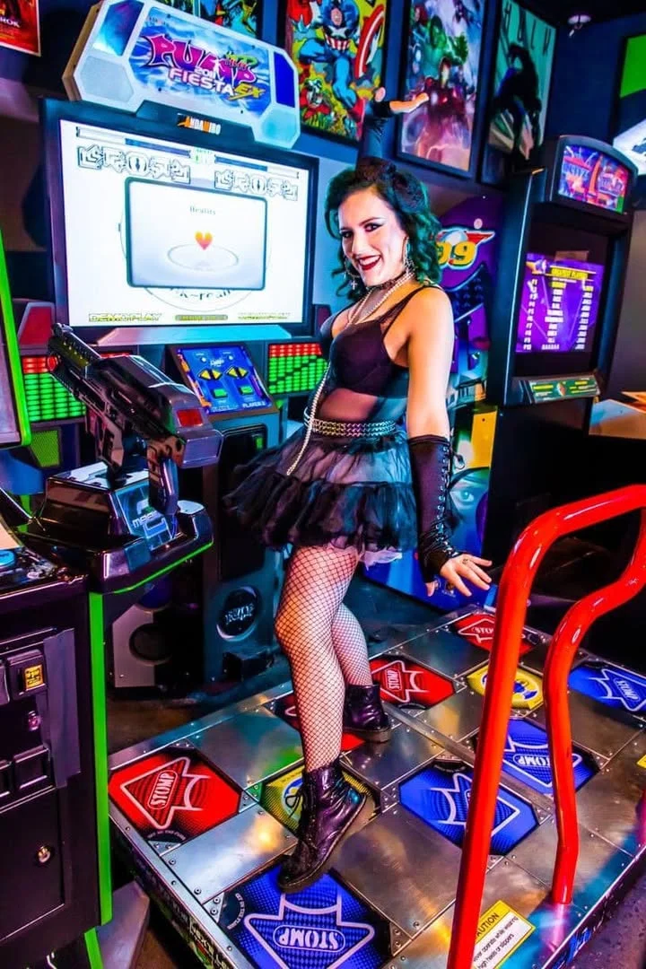 Woman in a black tutu posing in a vibrant arcade setting
