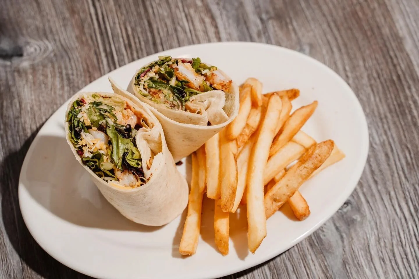 Grilled chicken wrap with fries on a white plate