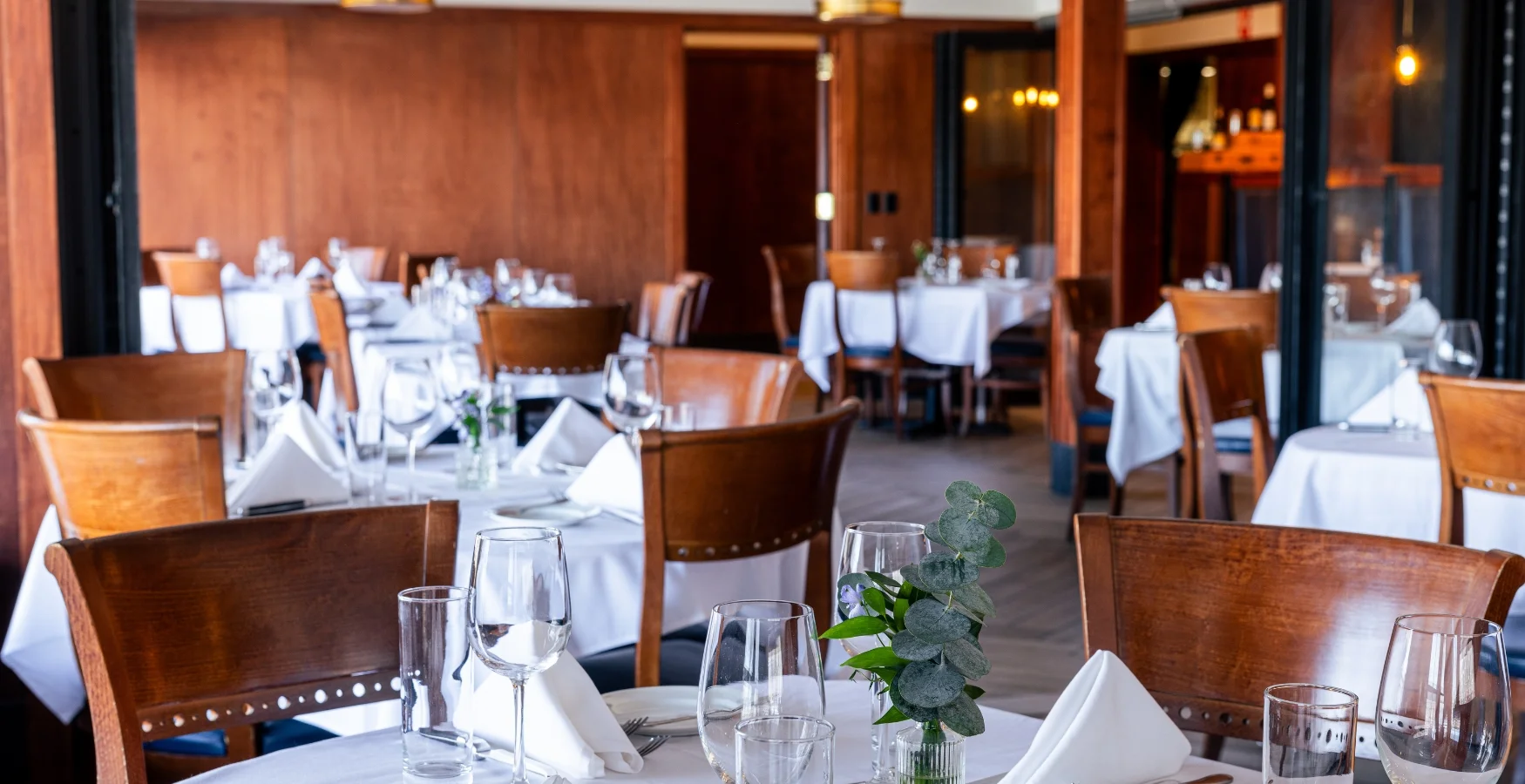 Dining room at Bass Street restaurant in downtown Moline, IL with wooden chairs and white linen napkins