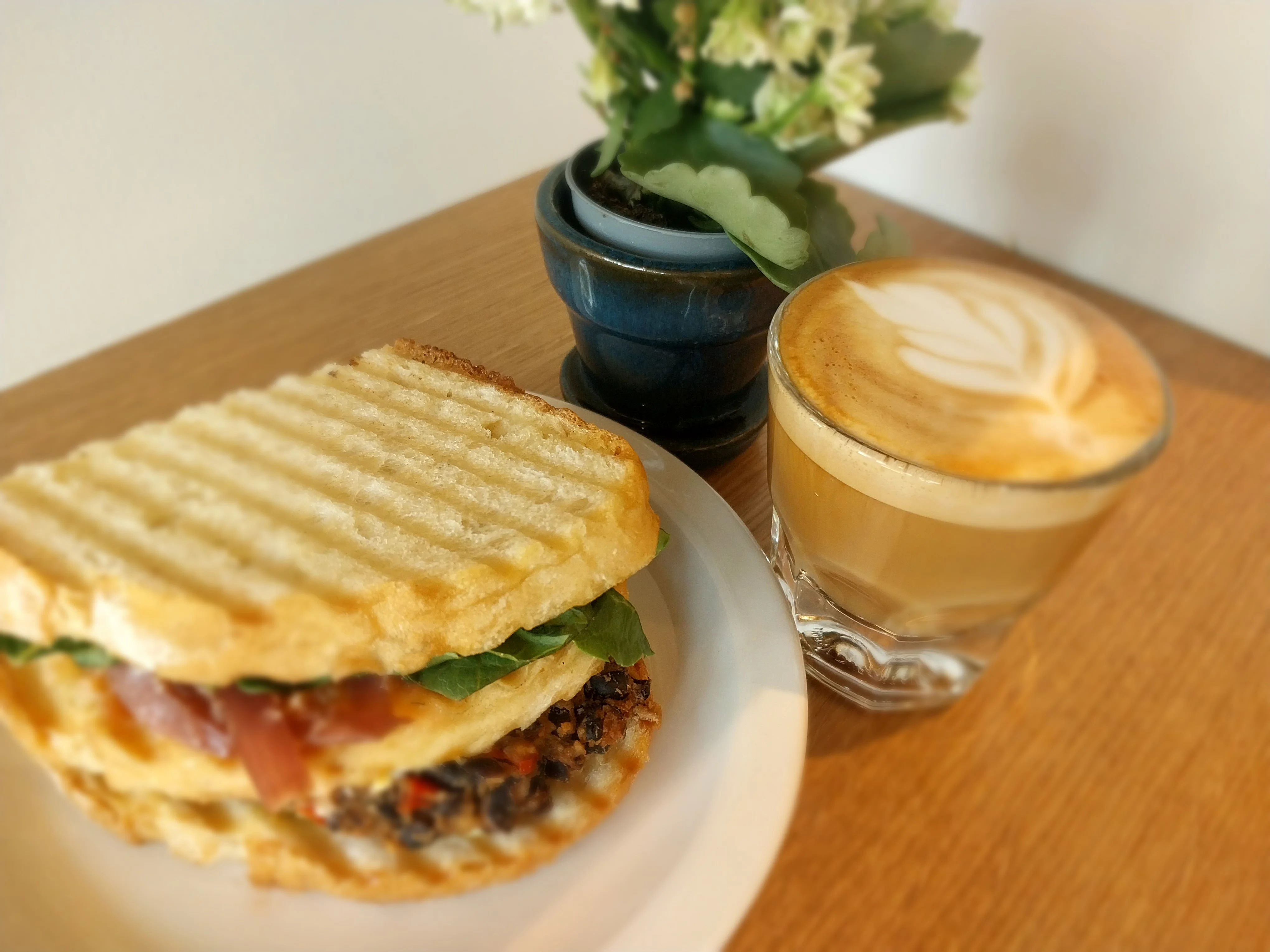 A toasted sandwich with greens and a latte on a wooden table.