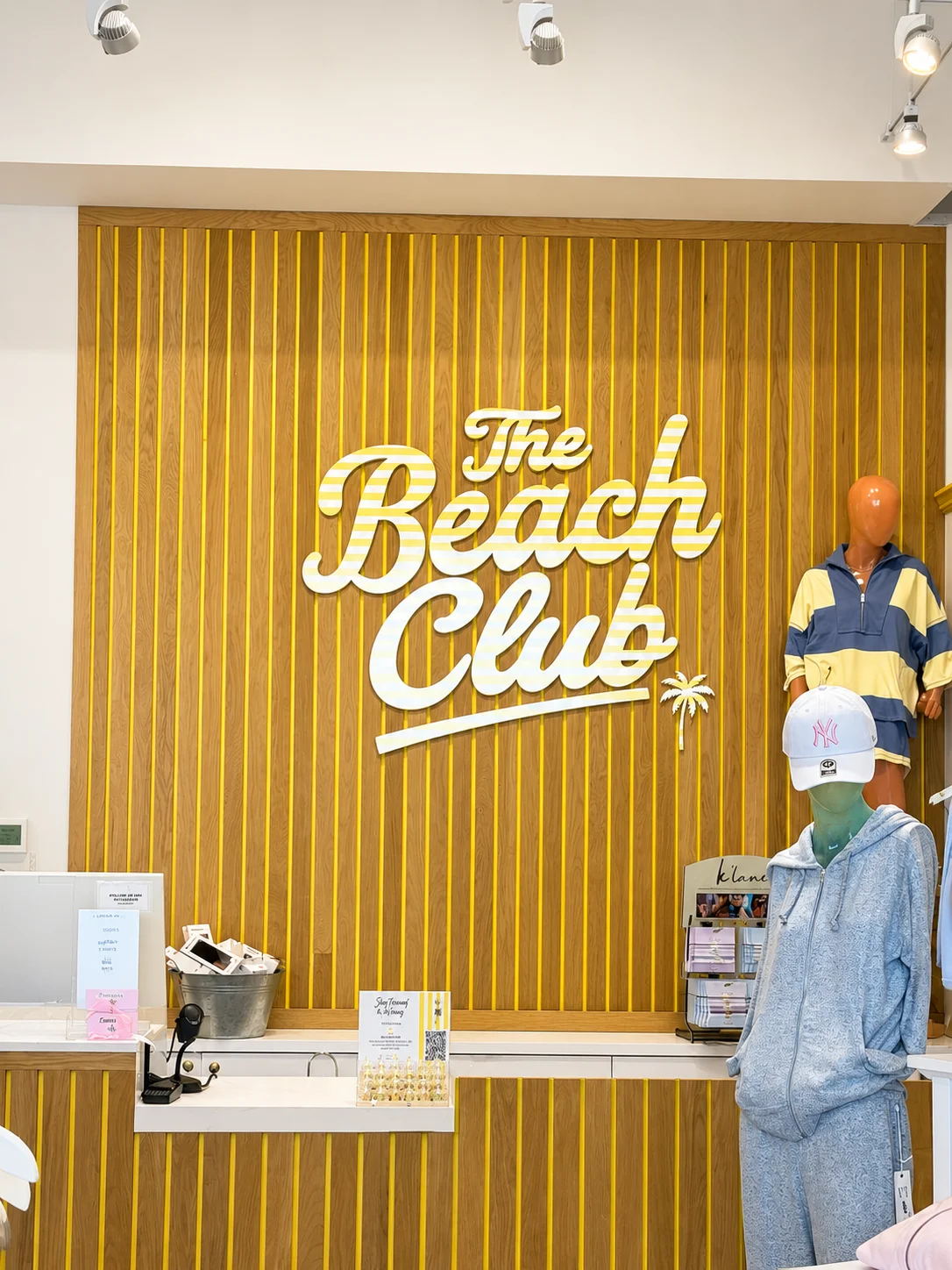 An interior view of The Beach Club store featuring a stylish sign and a clothing display. The decor includes wooden accents and vibrant colors.