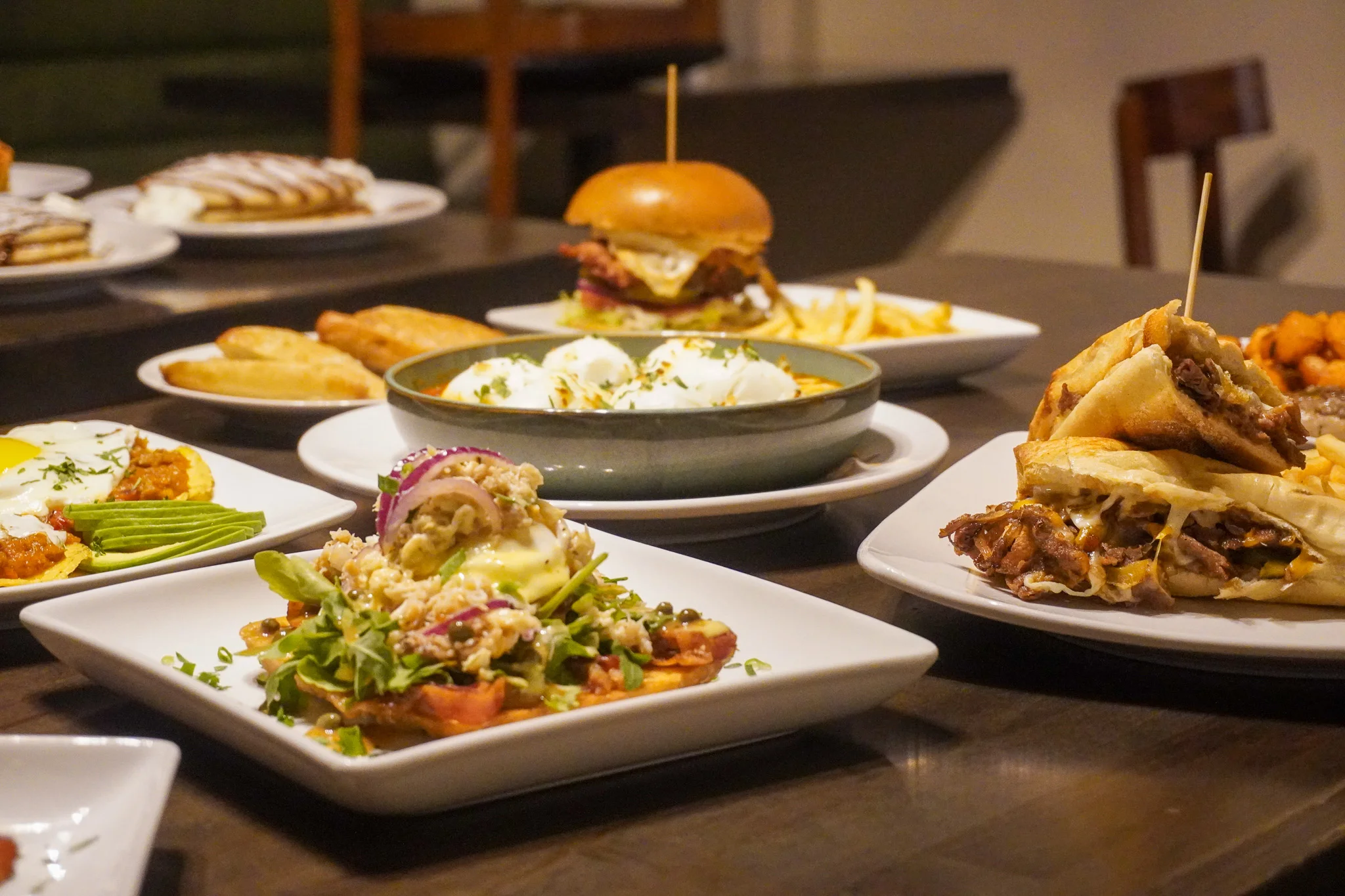 Assorted dishes including a burger, eggs, and salad in a restaurant setting