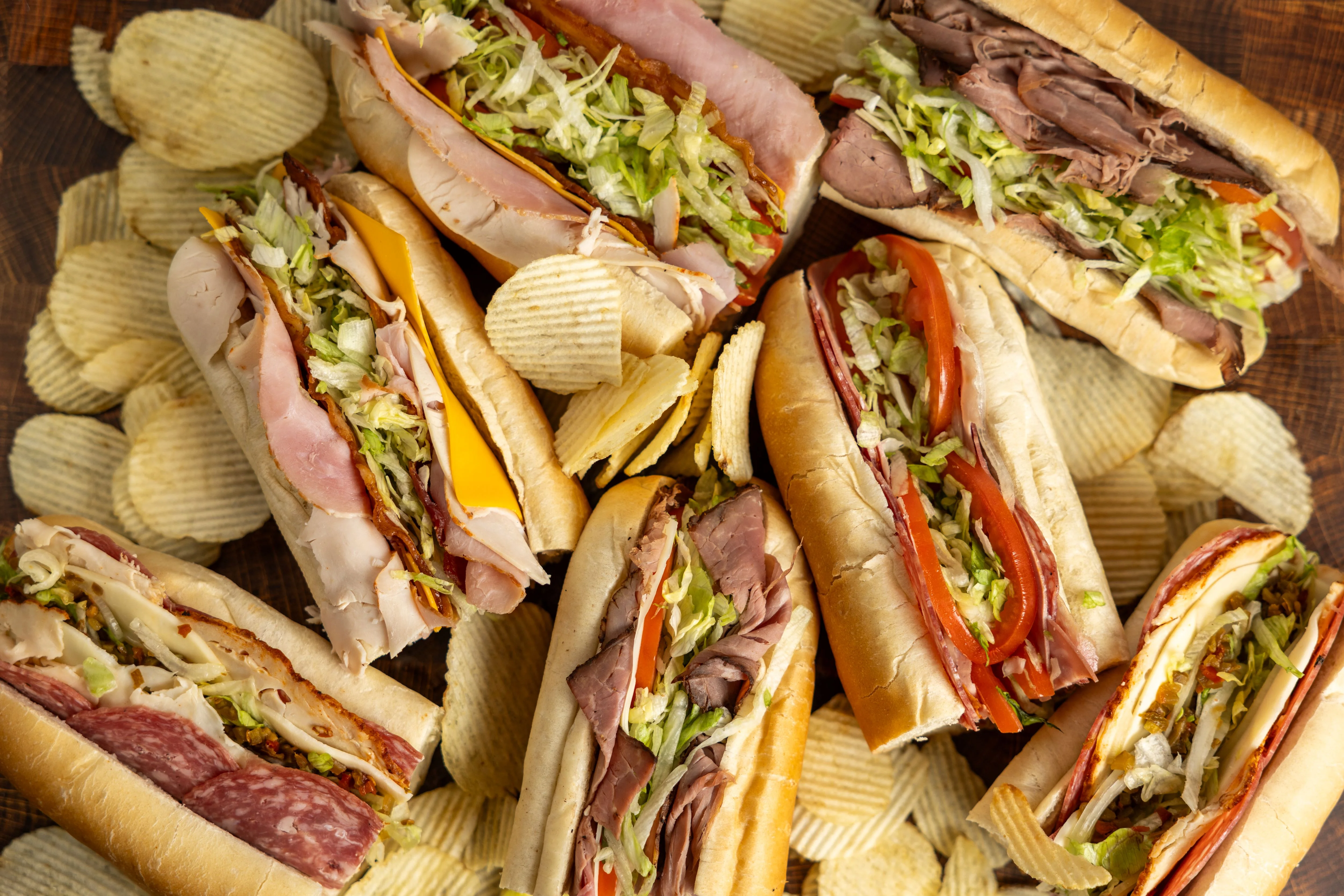 Assorted deli sandwiches with chips on a wooden board