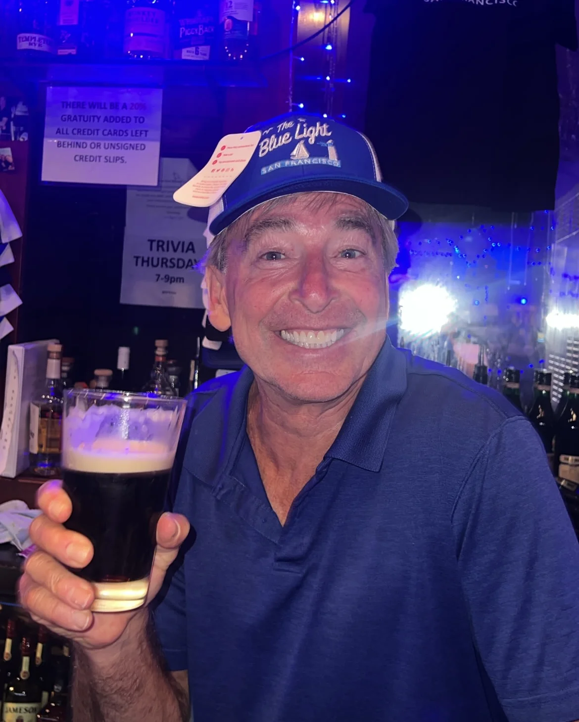 Bartender smiling with a pint of dark beer at a lively bar