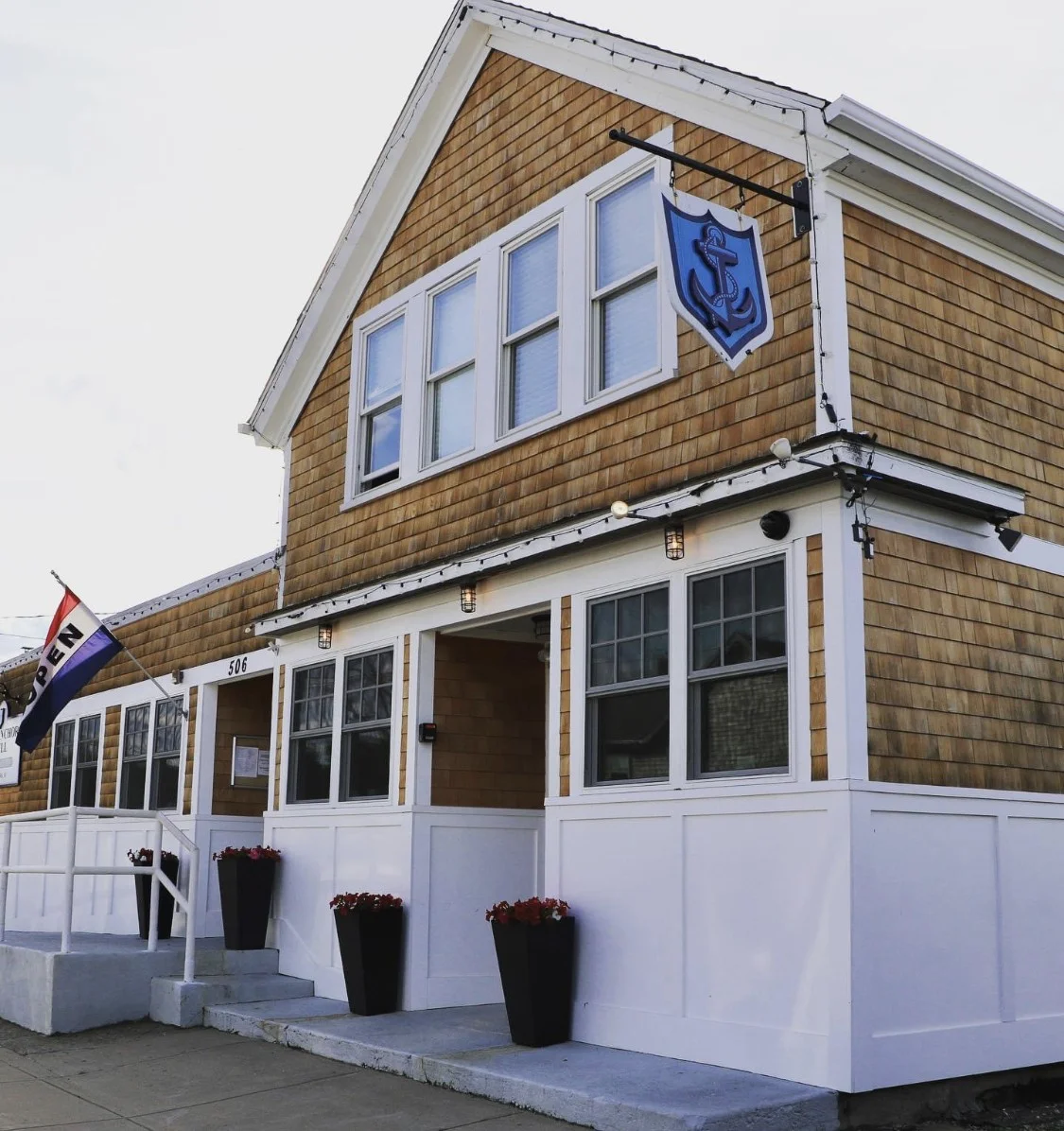 An exterior view of a charming restaurant building with wooden shingles and an 'open' flag displayed.