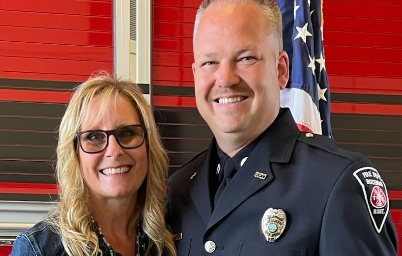 Two people smiling in front of a fire station backdrop
