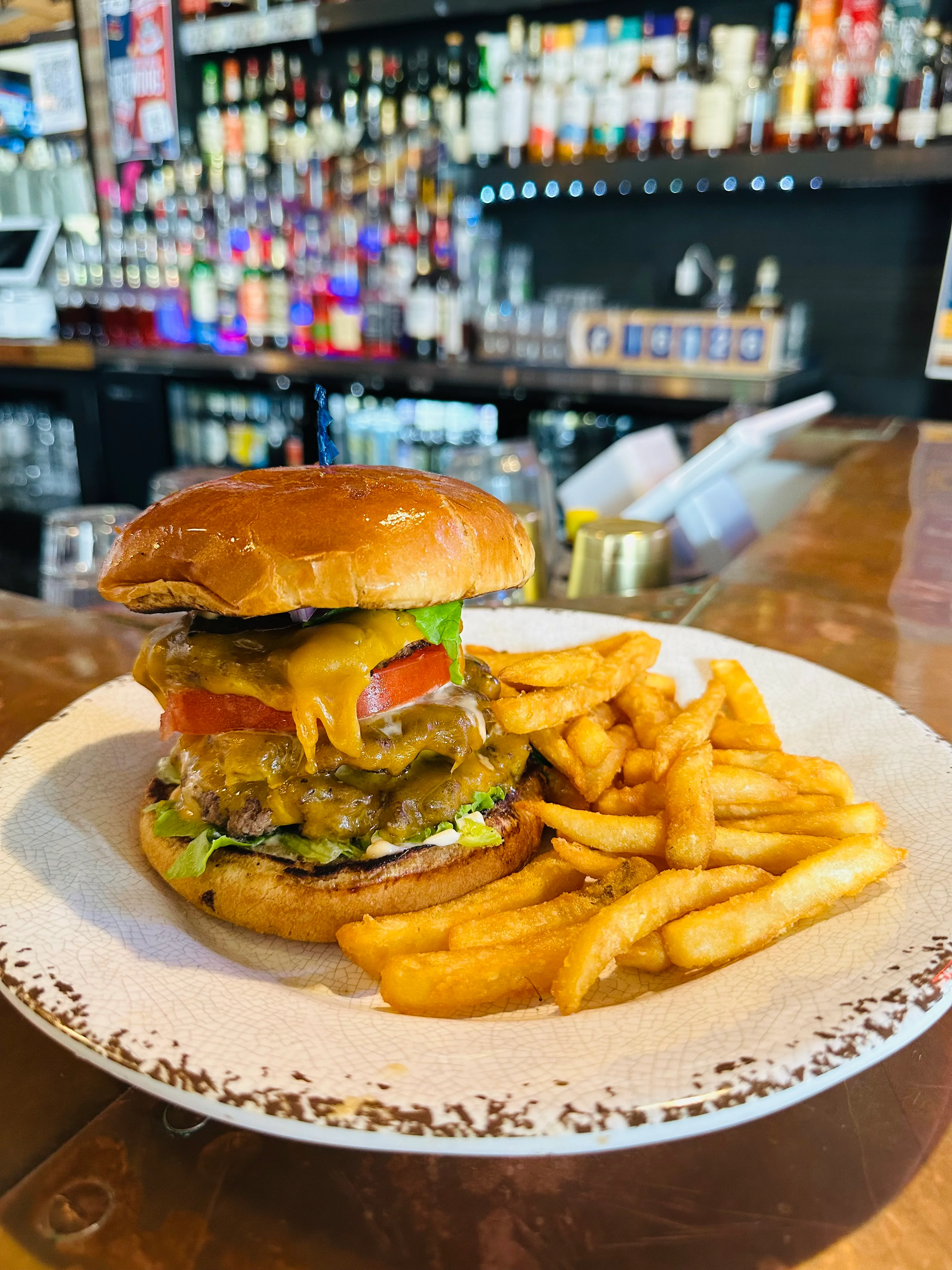A juicy burger stacked with cheese, lettuce, tomato, and pickles served with a side of crispy French fries on a decorative plate.