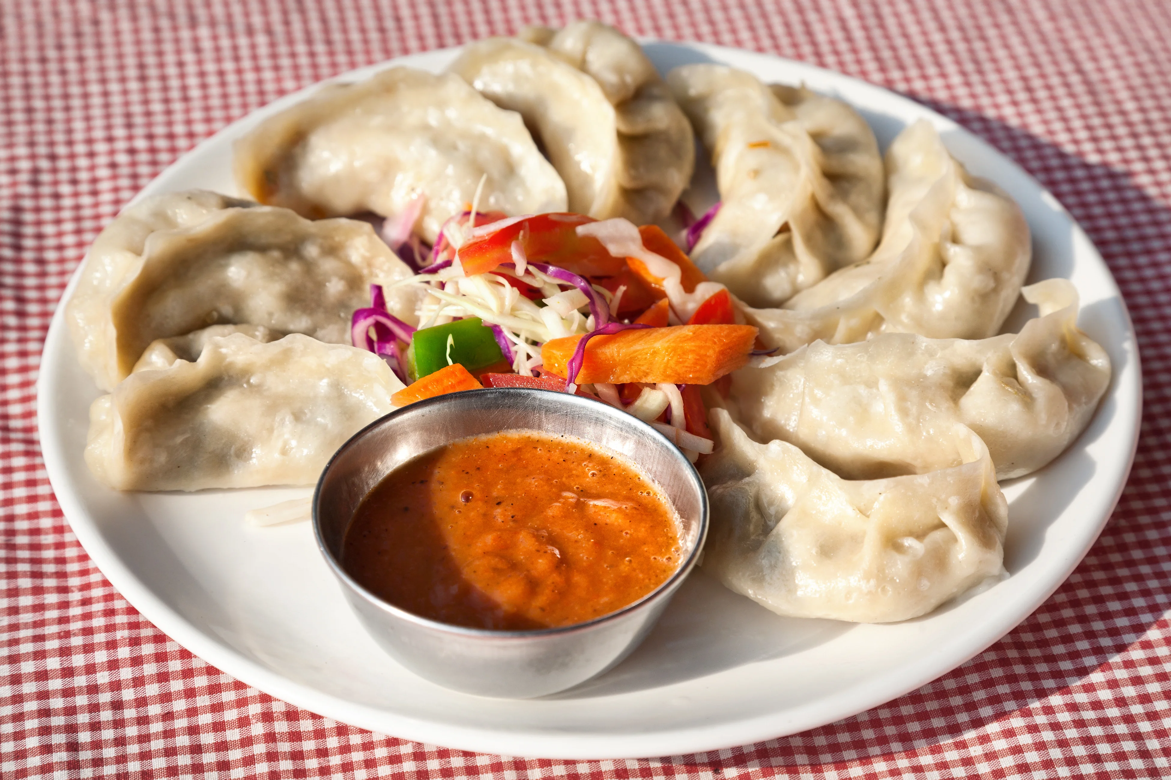 Plate of Nepali momos with dipping sauce and fresh vegetables